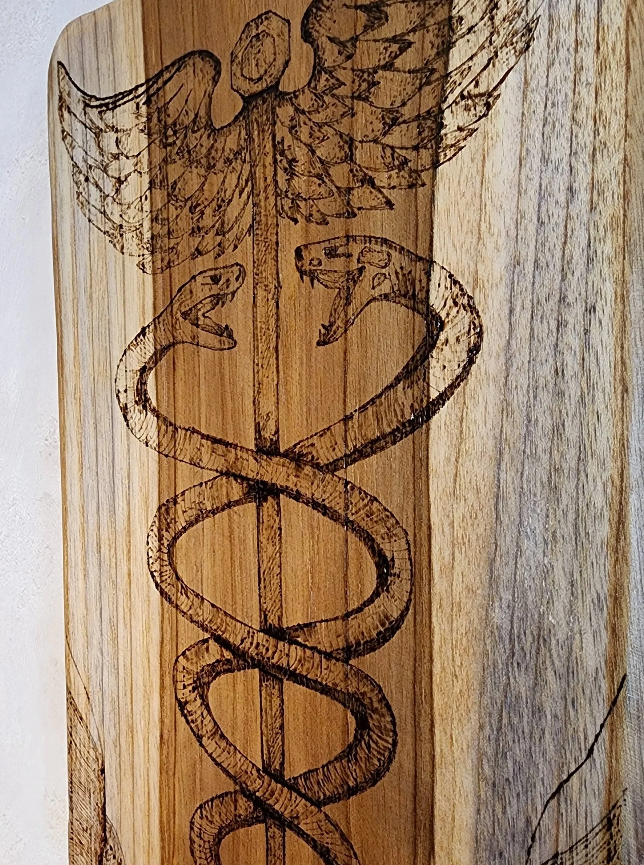 Bois pyrogravé représentant le symbole du caducée d'Hermès. Elaura Donnadieu, graphiste, illustratrice et artiste peintre.