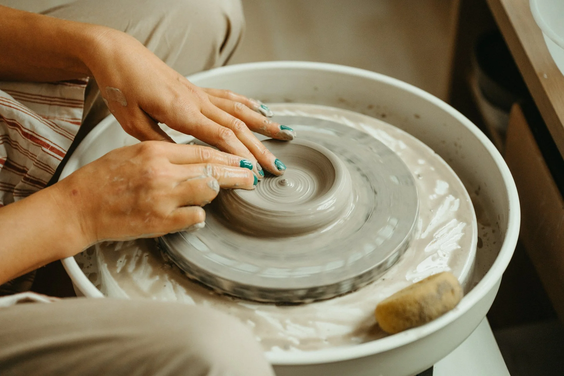 Person shaping wet clay on a pottery wheel in a pottery studio.