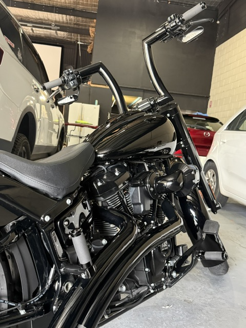 Black motorcycle with a low seat, high handlebars, and chrome accents inside a garage with cars parked nearby. Detailing service at Tweed Dent Repairs