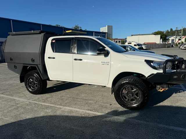 White pickup truck with a custom black canopy parked in a parking lot on a sunny day. A service from Tweed Dent Repairs