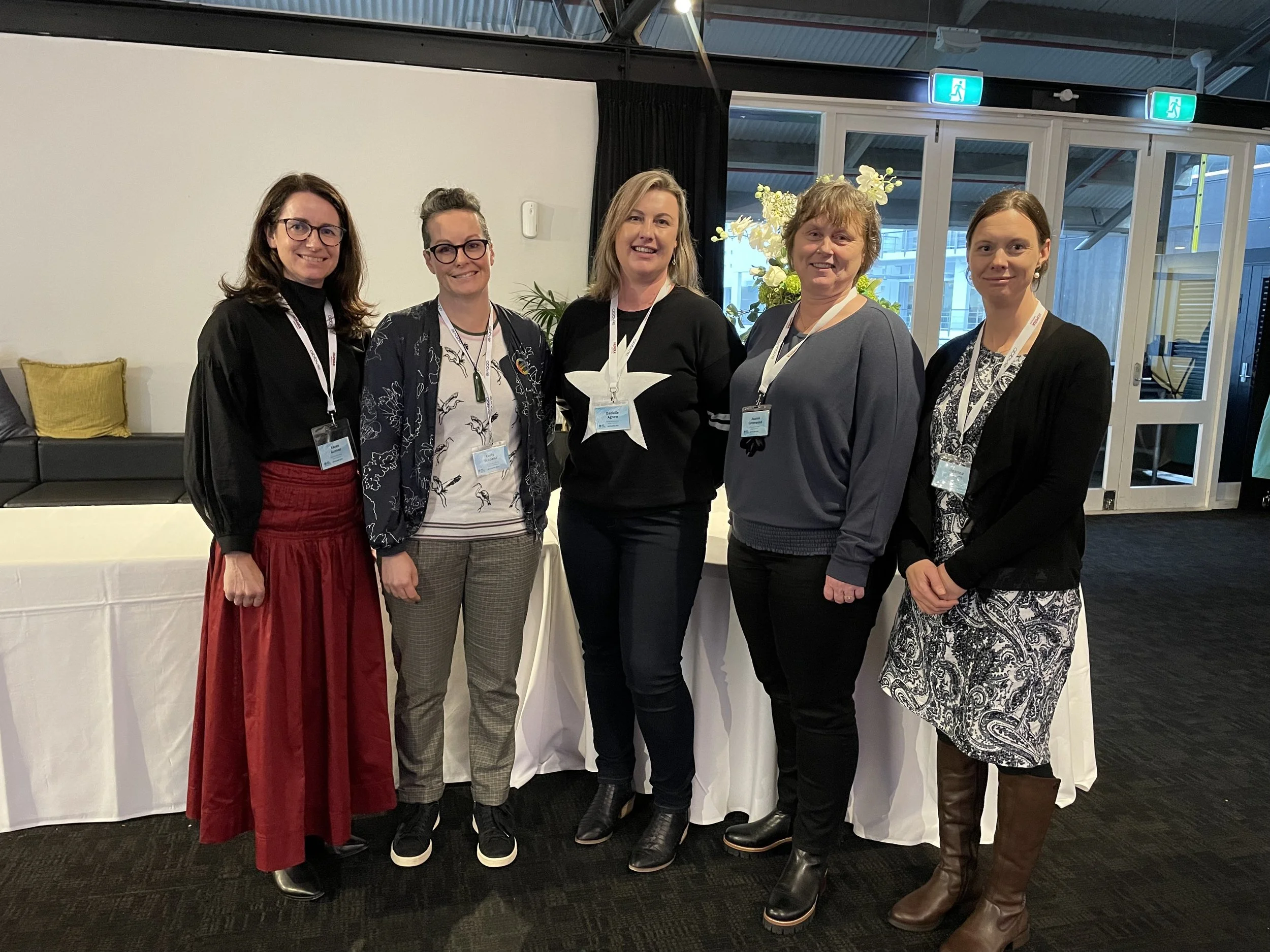 Group of five women standing together at a conference, wearing badges and smiling.