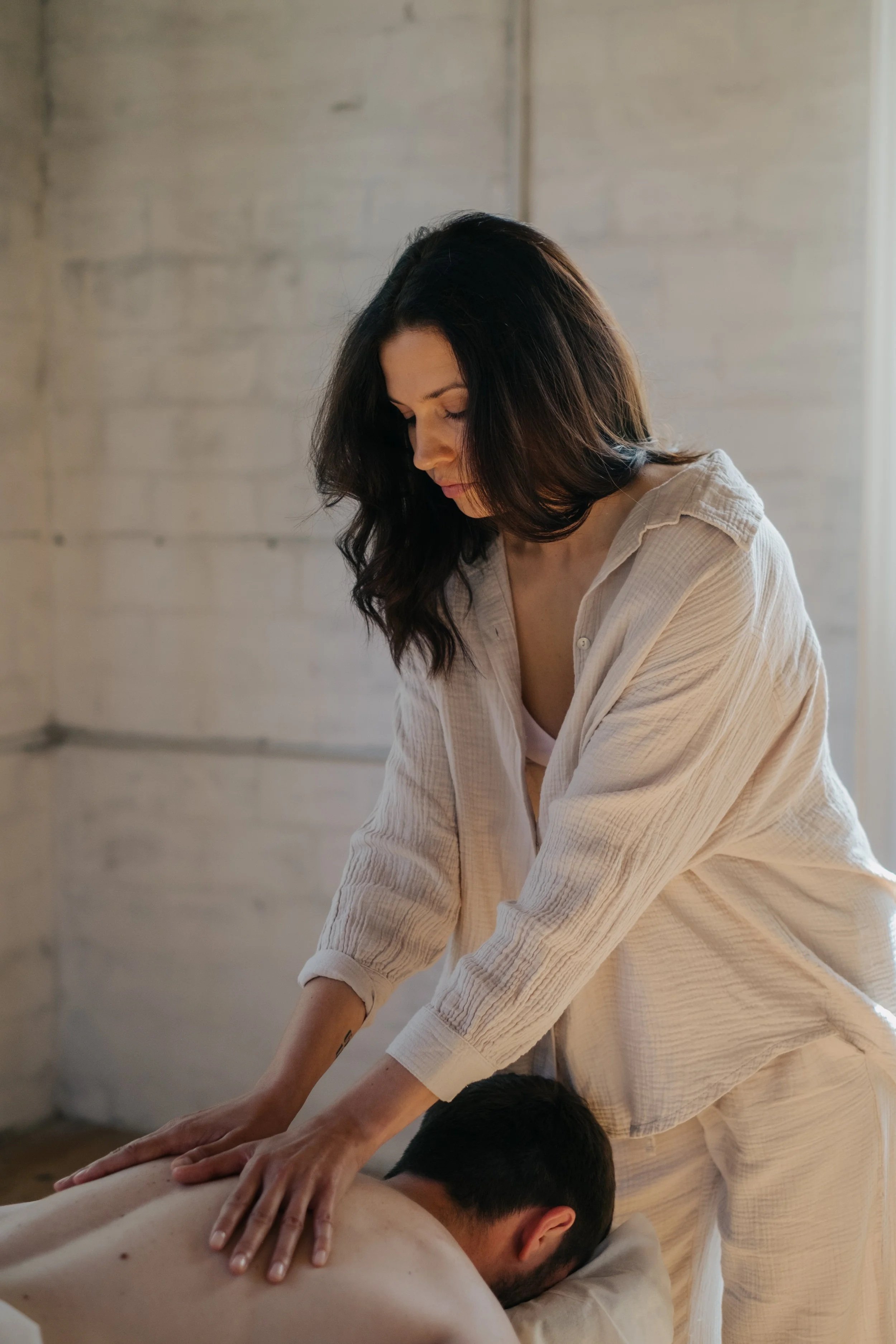 Frau gibt einem Mann eine Massage in einem hellen Raum und weißem Wandhintergrund.