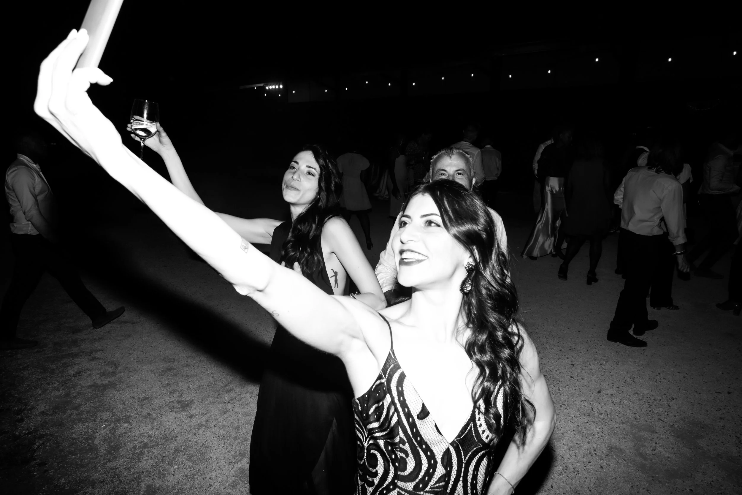 People dancing at a party or celebration, with two women in the foreground and others in the background, black and white photo.