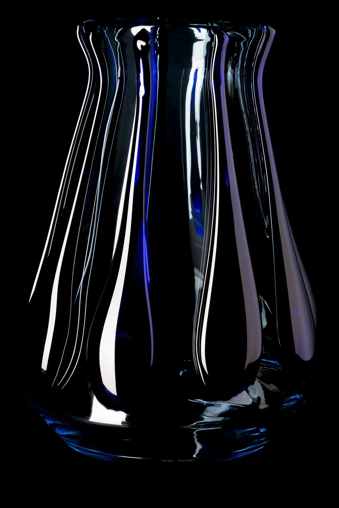 A black glass vase with vertical ridges, reflecting blue and white light, set against a black background.