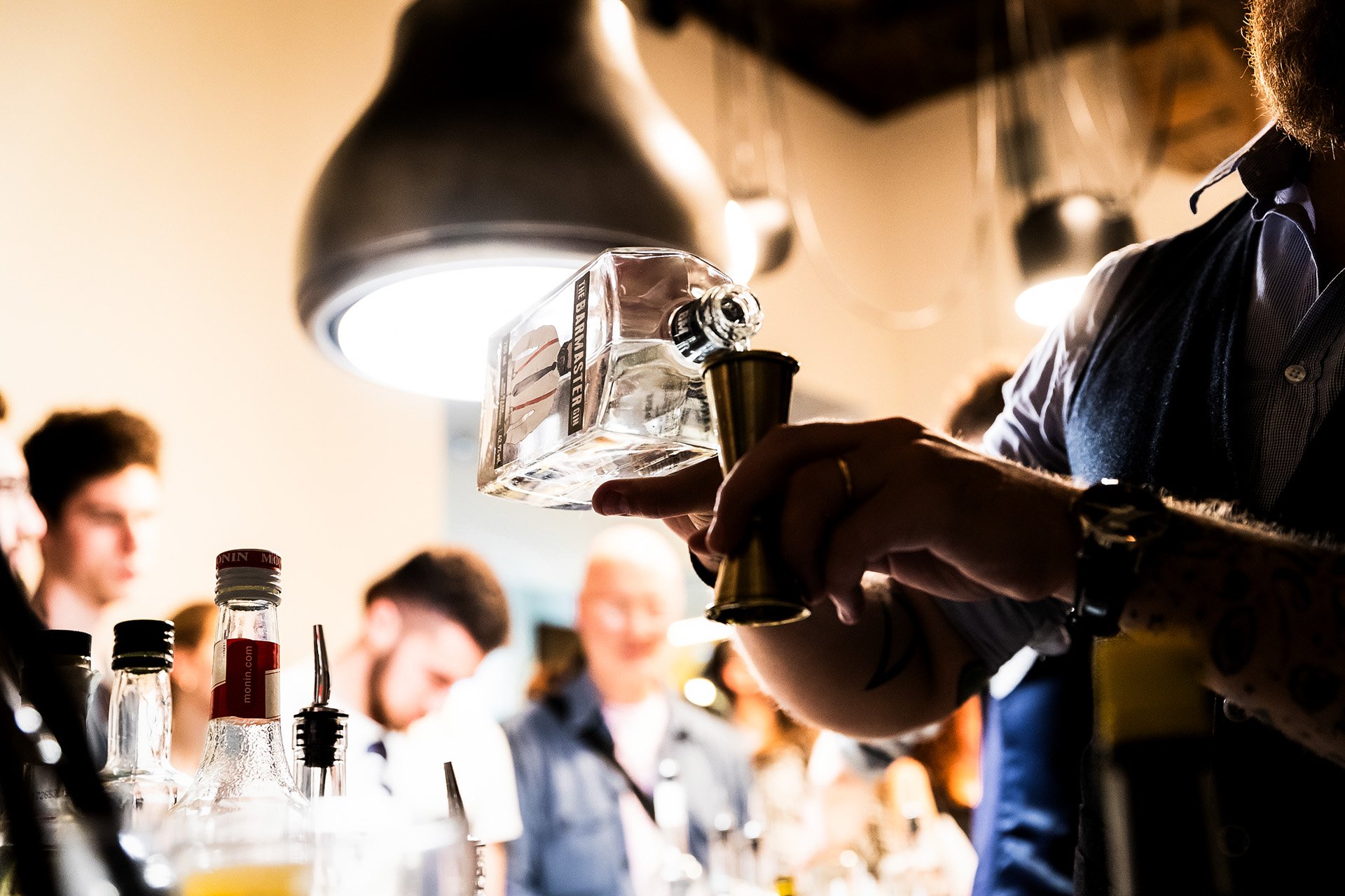 Bartender pouring alcohol into a shot glass at a crowded bar