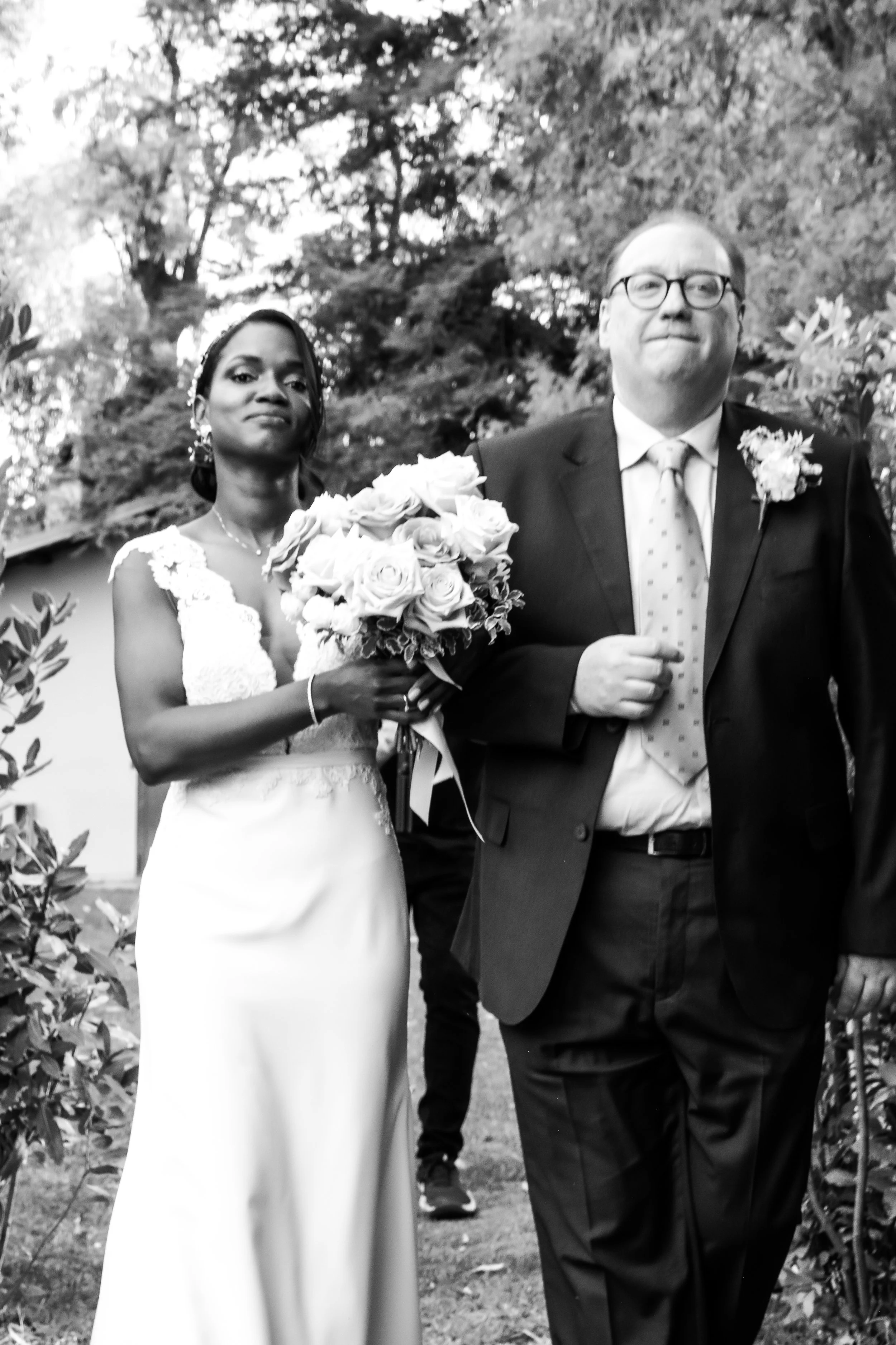 A bride in a wedding dress holding a bouquet of roses and a groom in a suit walking outdoors.