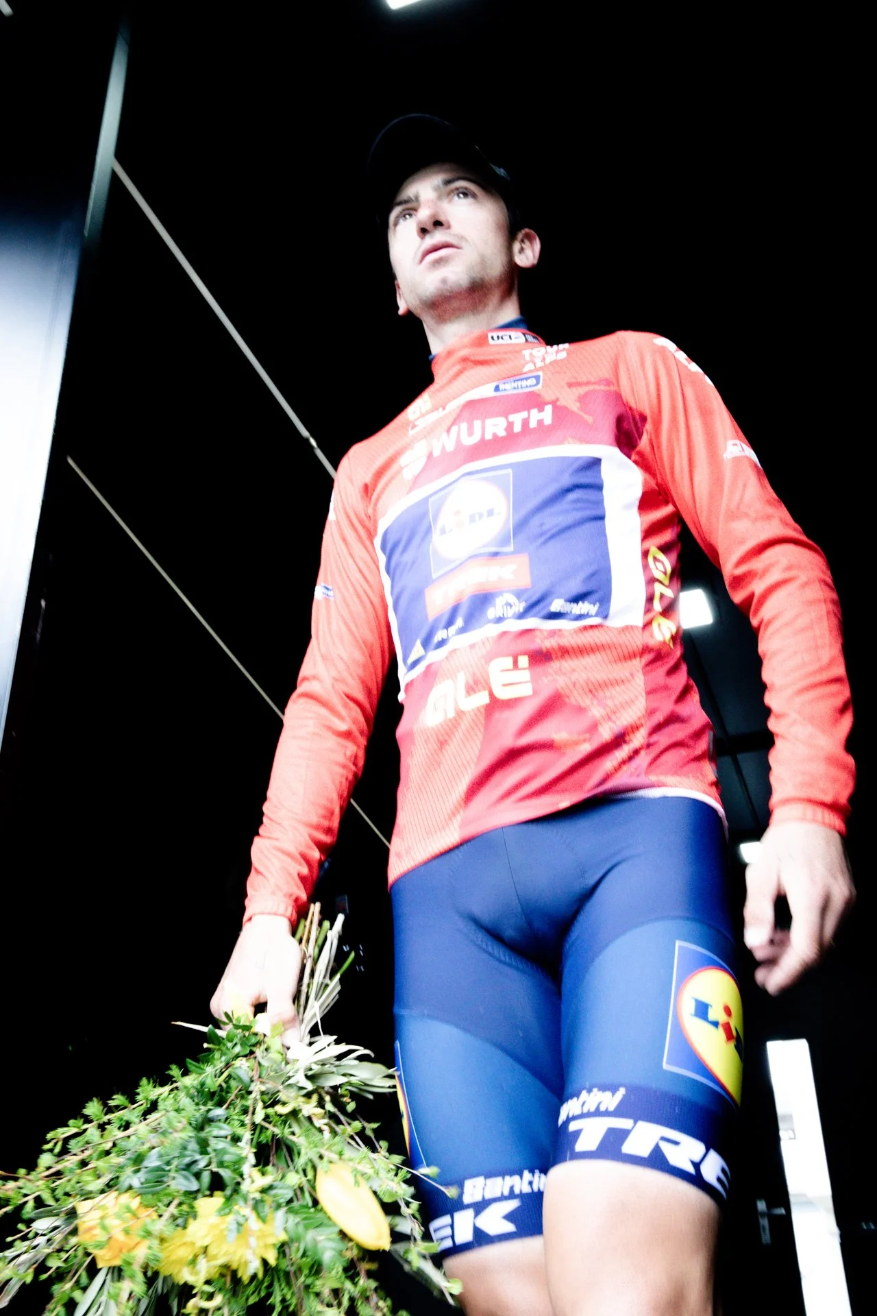 A male cyclist wearing a red and blue racing outfit holding a bouquet of flowers.