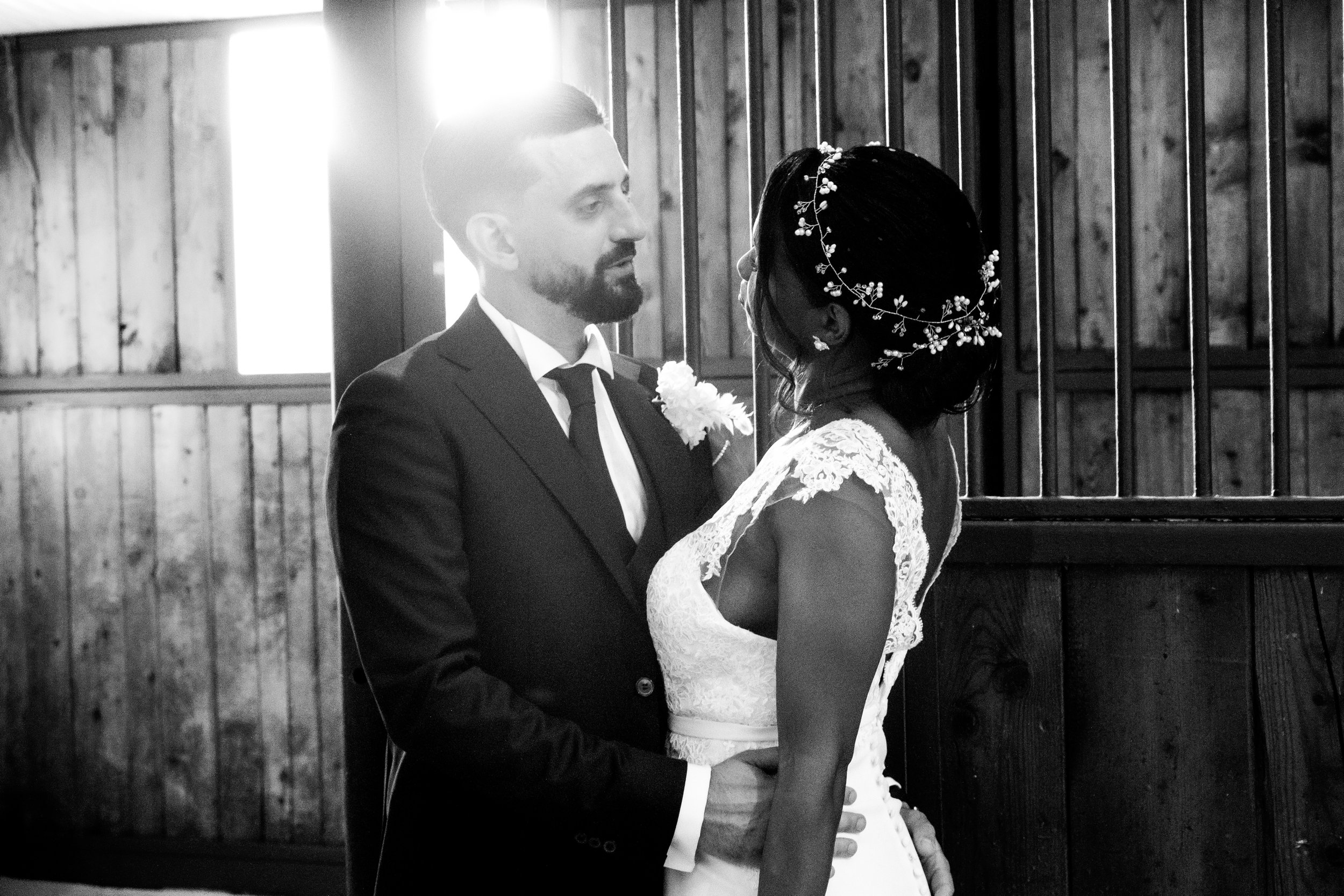 A black and white photo of a bride and groom standing closely during their wedding ceremony inside a wooden building, facing each other, with the groom holding the bride's waist.