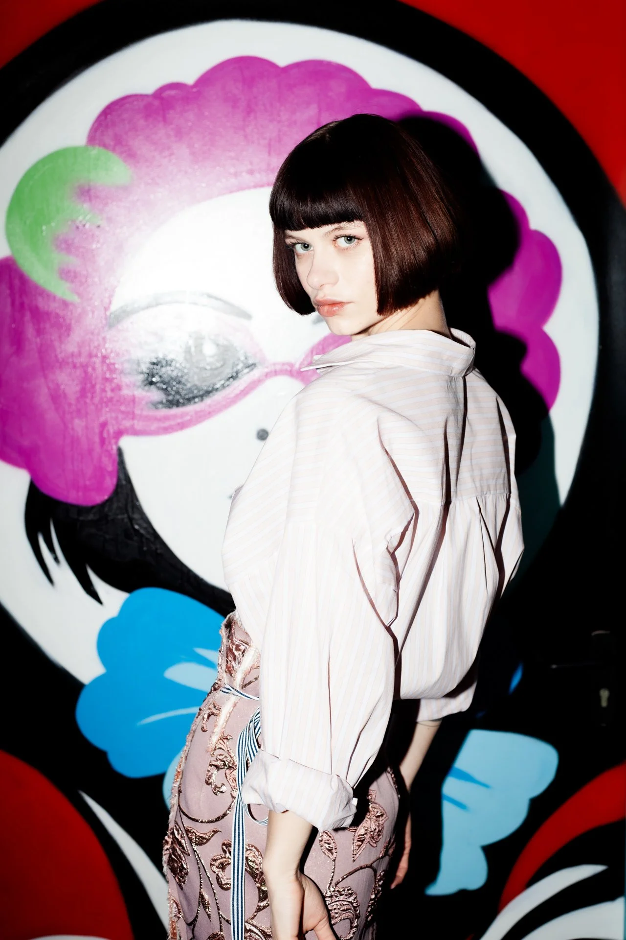 A woman with short dark hair and a striped shirt standing in front of a colorful, abstract mural painting.