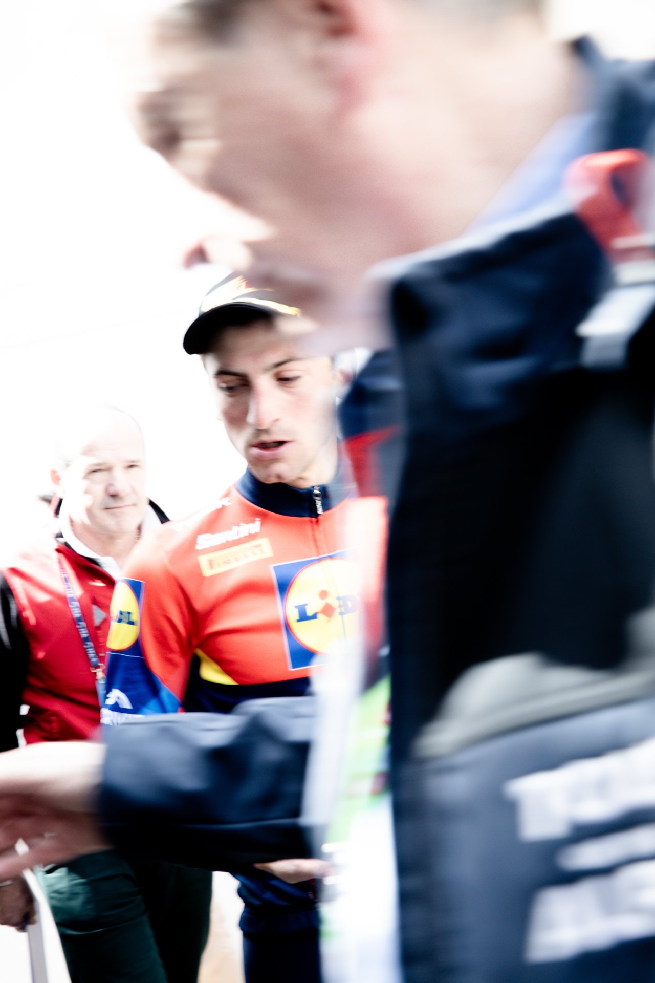Men in racing team uniforms standing together, exchanging items, with a bright background.