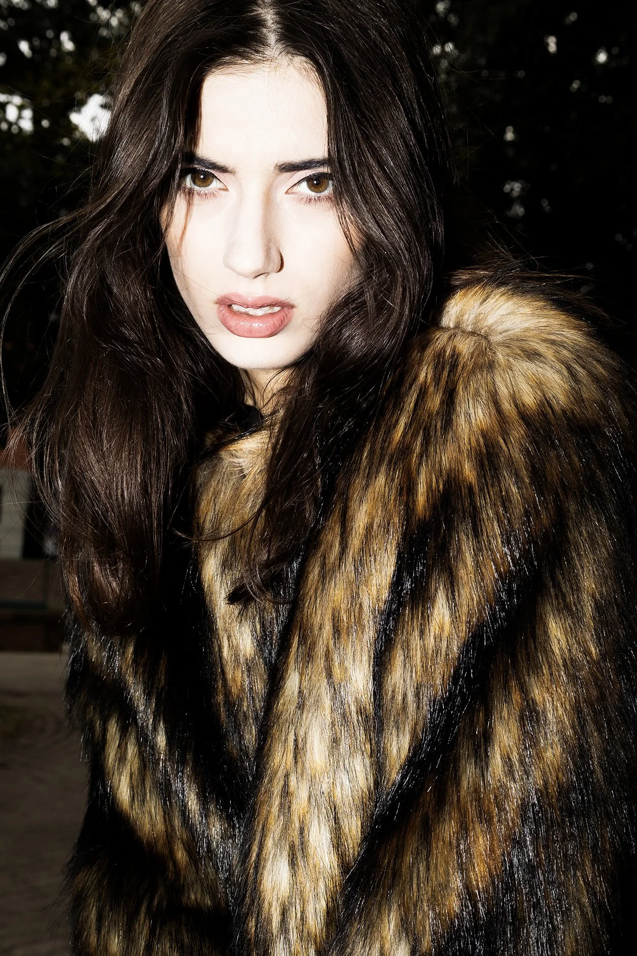 Portrait of a young woman with long dark hair, fair skin, and brown eyes, wearing a fur coat outdoors.
