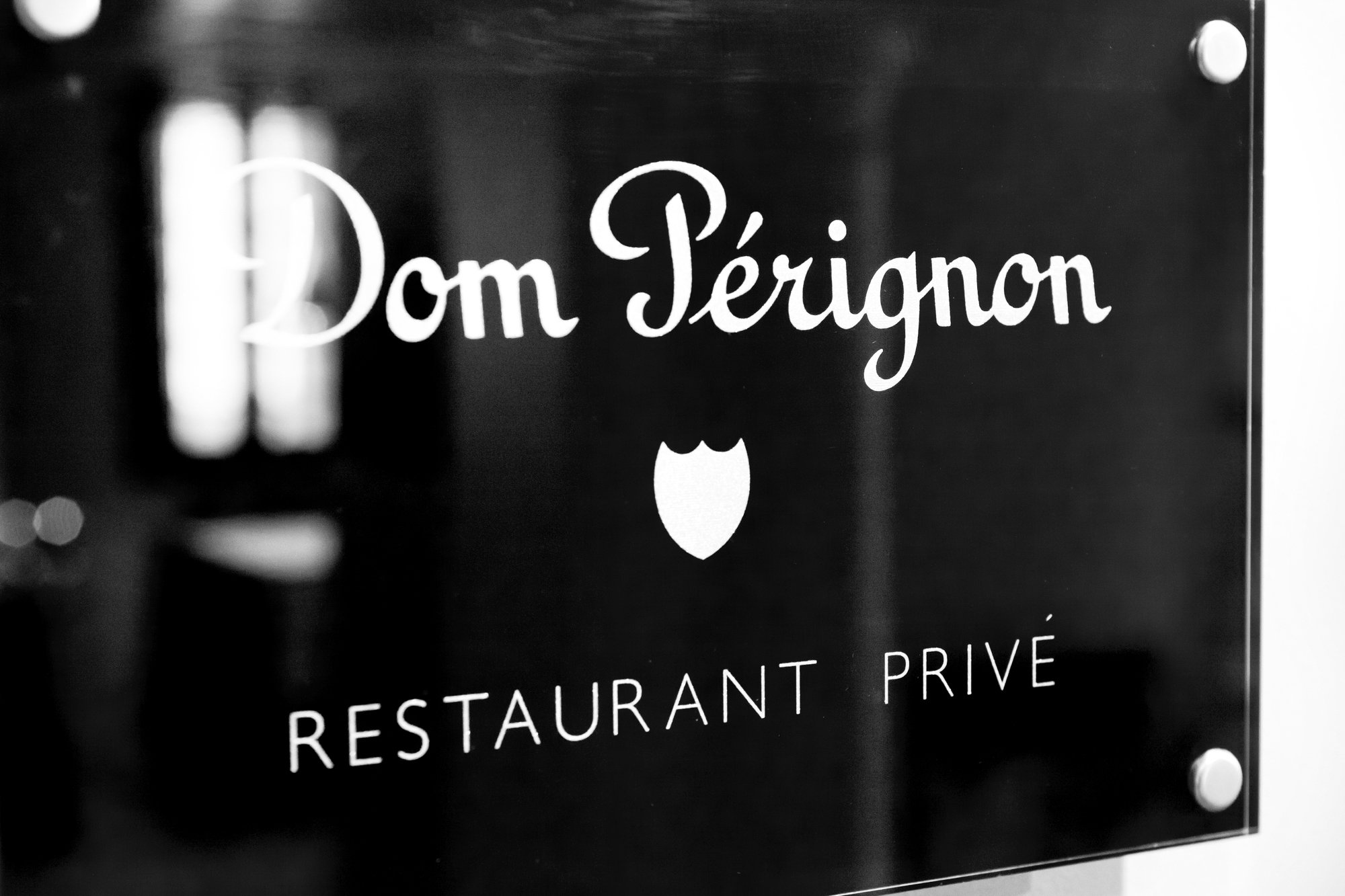 Close-up of a black sign with white lettering reading 'Dom Pérignon' and 'Restaurant Privé' with a small logo of a shield in the center.