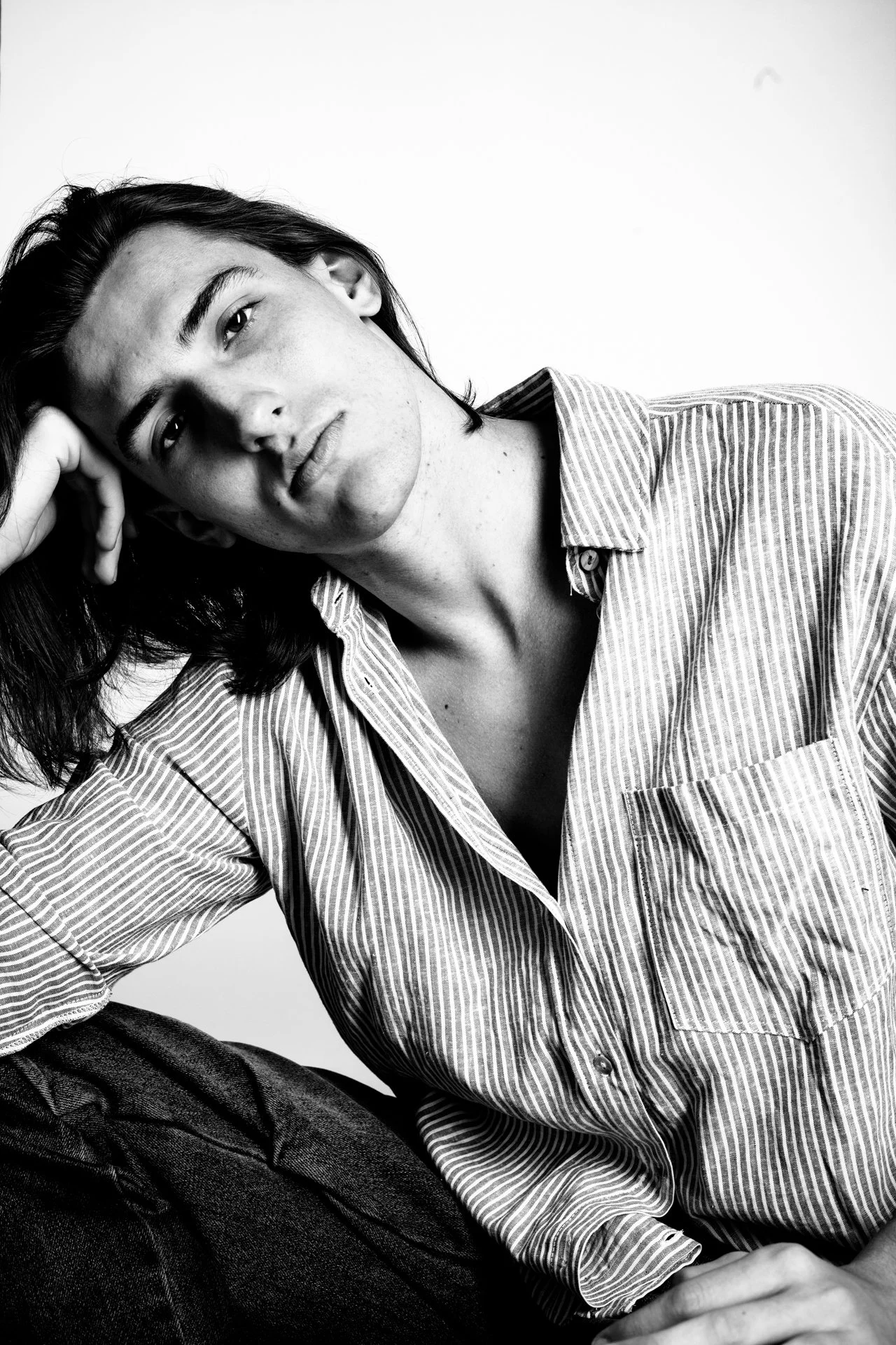 Black and white portrait of a young woman with dark hair, wearing a striped shirt, resting her head on her hand with a neutral expression.