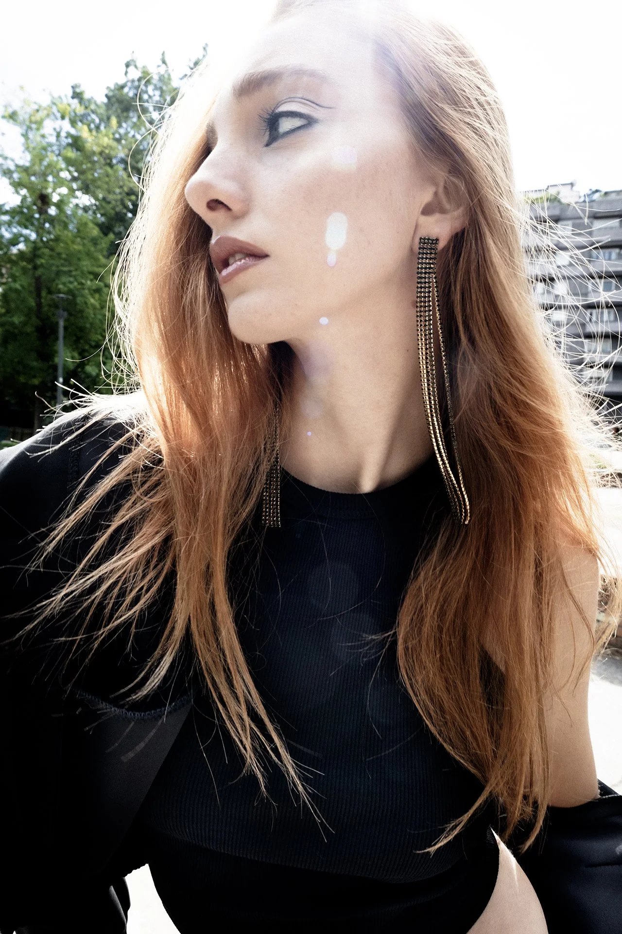 A woman with red hair and large earrings looking away in sunlight outdoors.