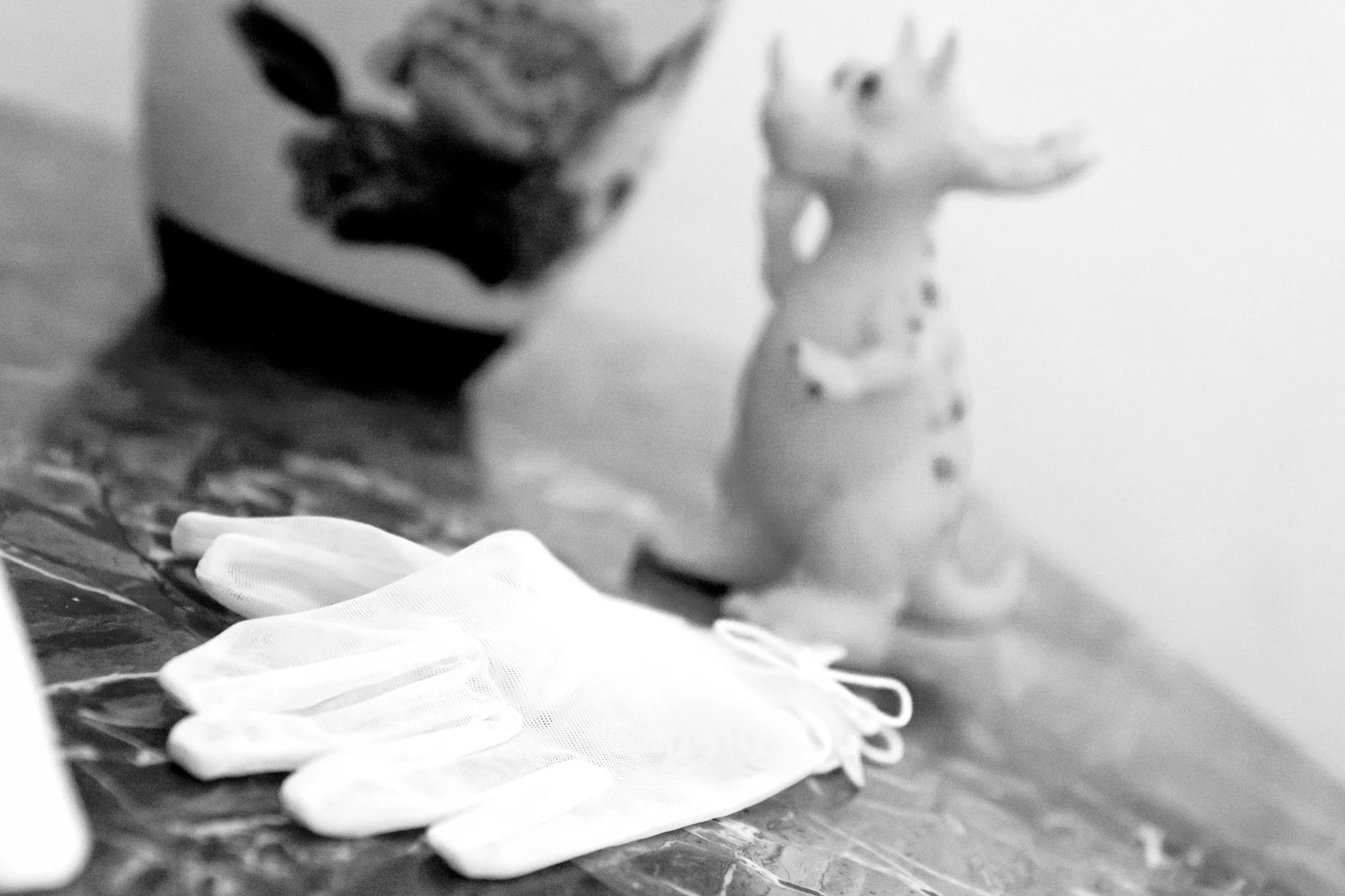 A pair of white disposable gloves resting on a table, with a toy giraffe in the background and a container with what appears to be a painted animal face.
