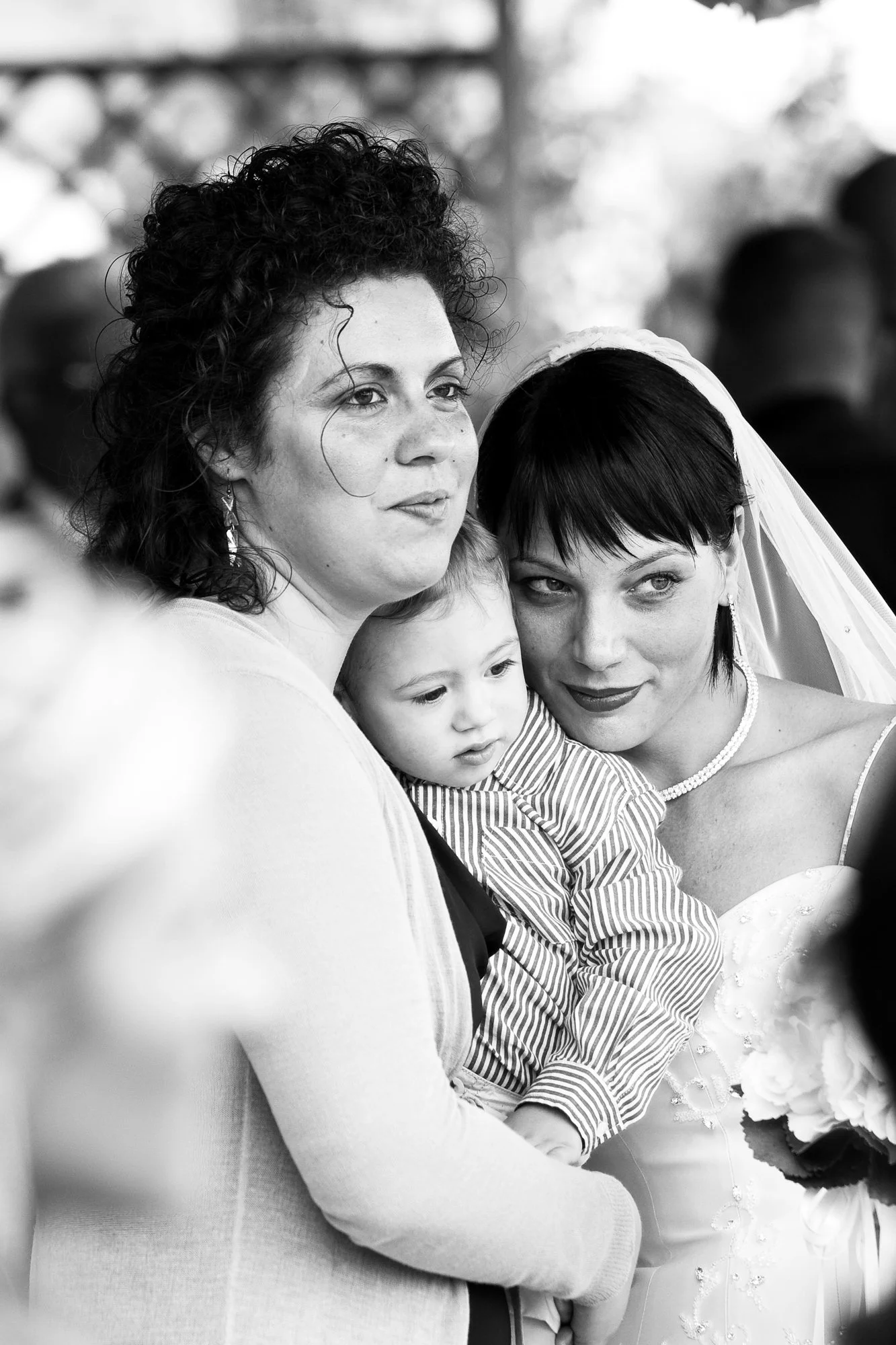 Black and white photo of three women and a young boy sharing emotional moments, with one woman dressed in a wedding gown.