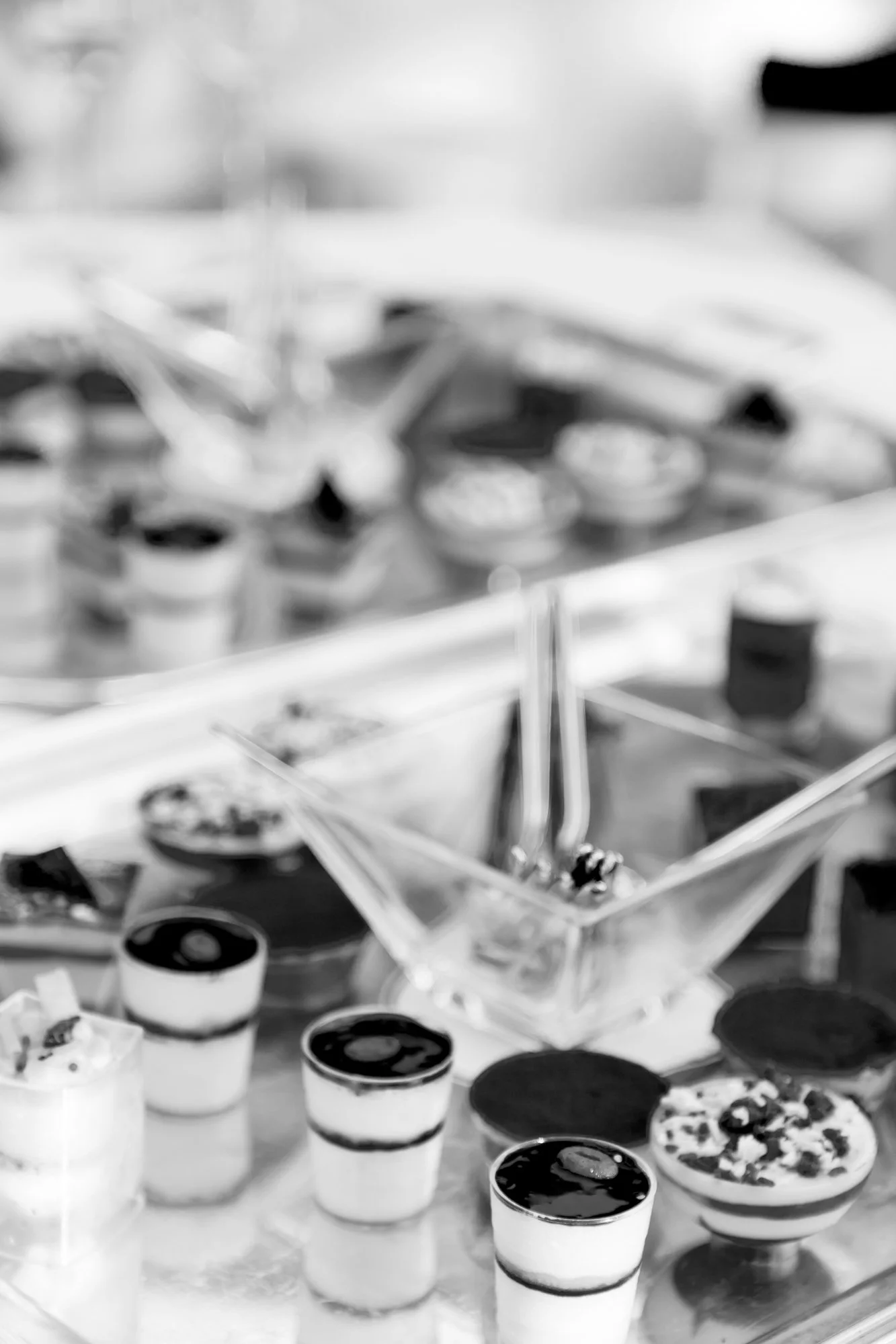 A display of assorted small desserts, including parfaits, tarts, and other baked goods, set on a reflective surface in a bakery or cafe setting.