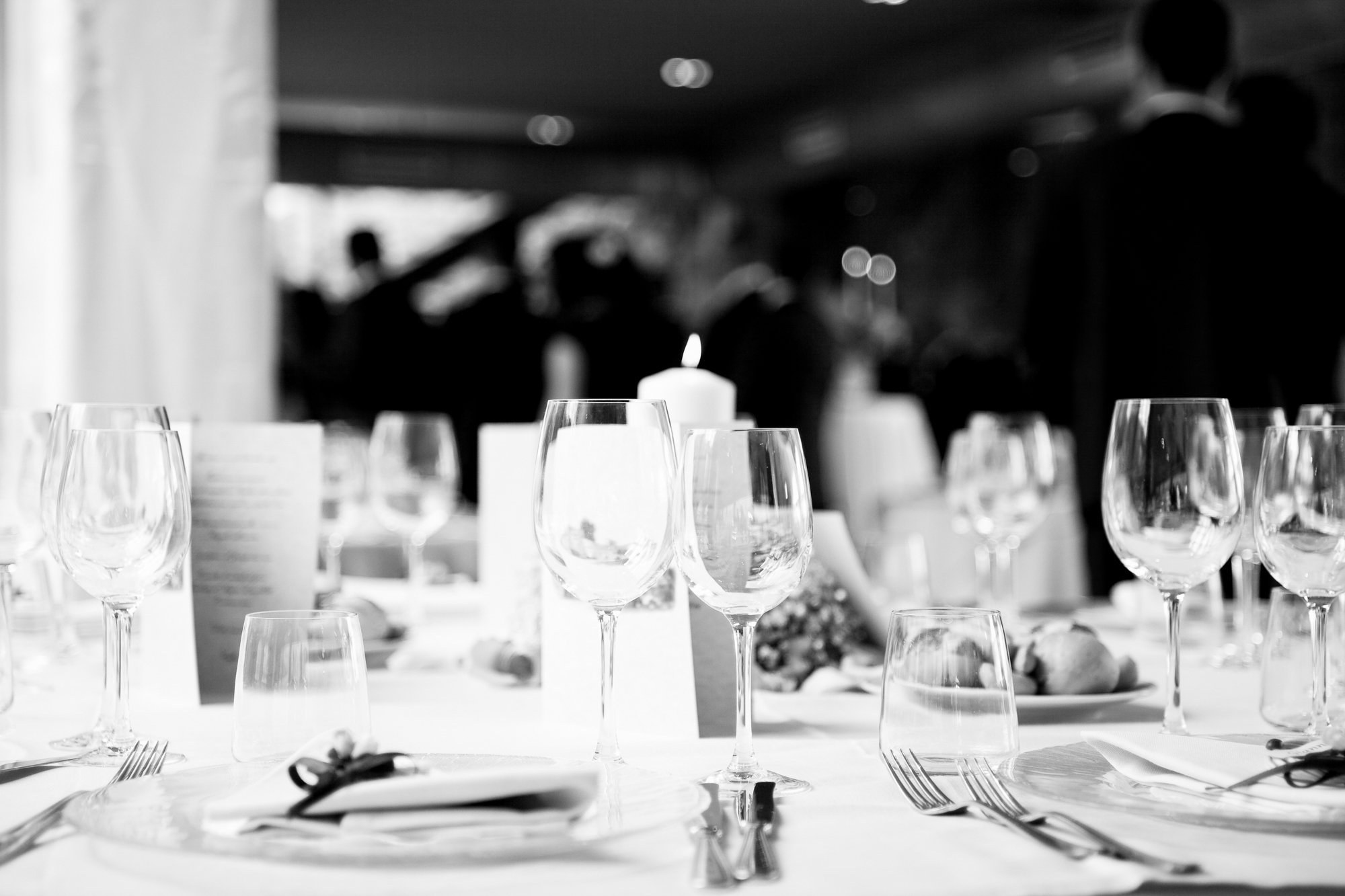 A table set with wine glasses, water glasses, plates, silverware, and a candle in the background at an elegant event.