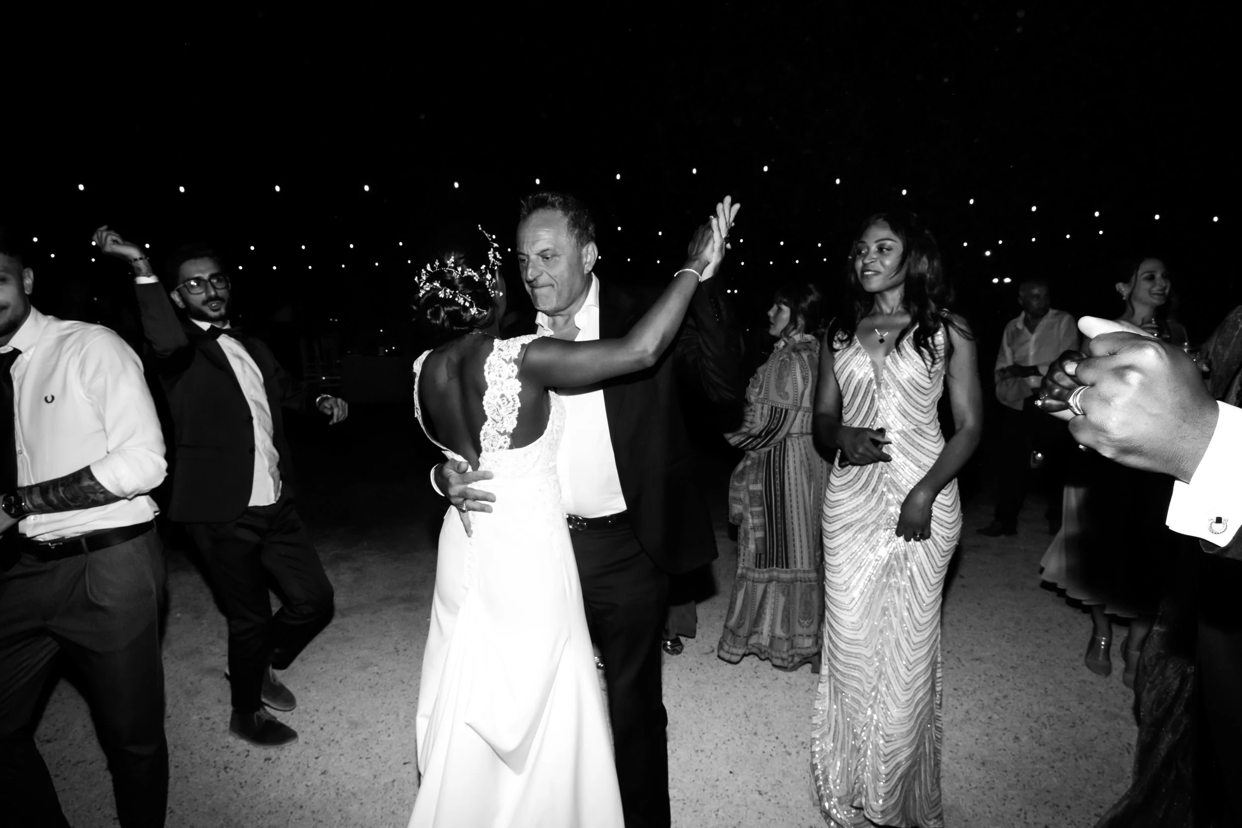 People dancing at a celebration or wedding reception, with a couple in the center dancing closely and others around watching and enjoying.