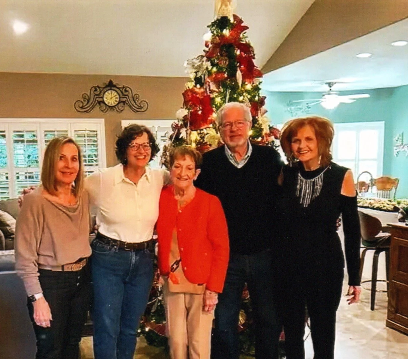 A group of five people, three women and two men, standing together in a living room in front of a decorated Christmas tree, smiling and posing for a photo during a holiday gathering.