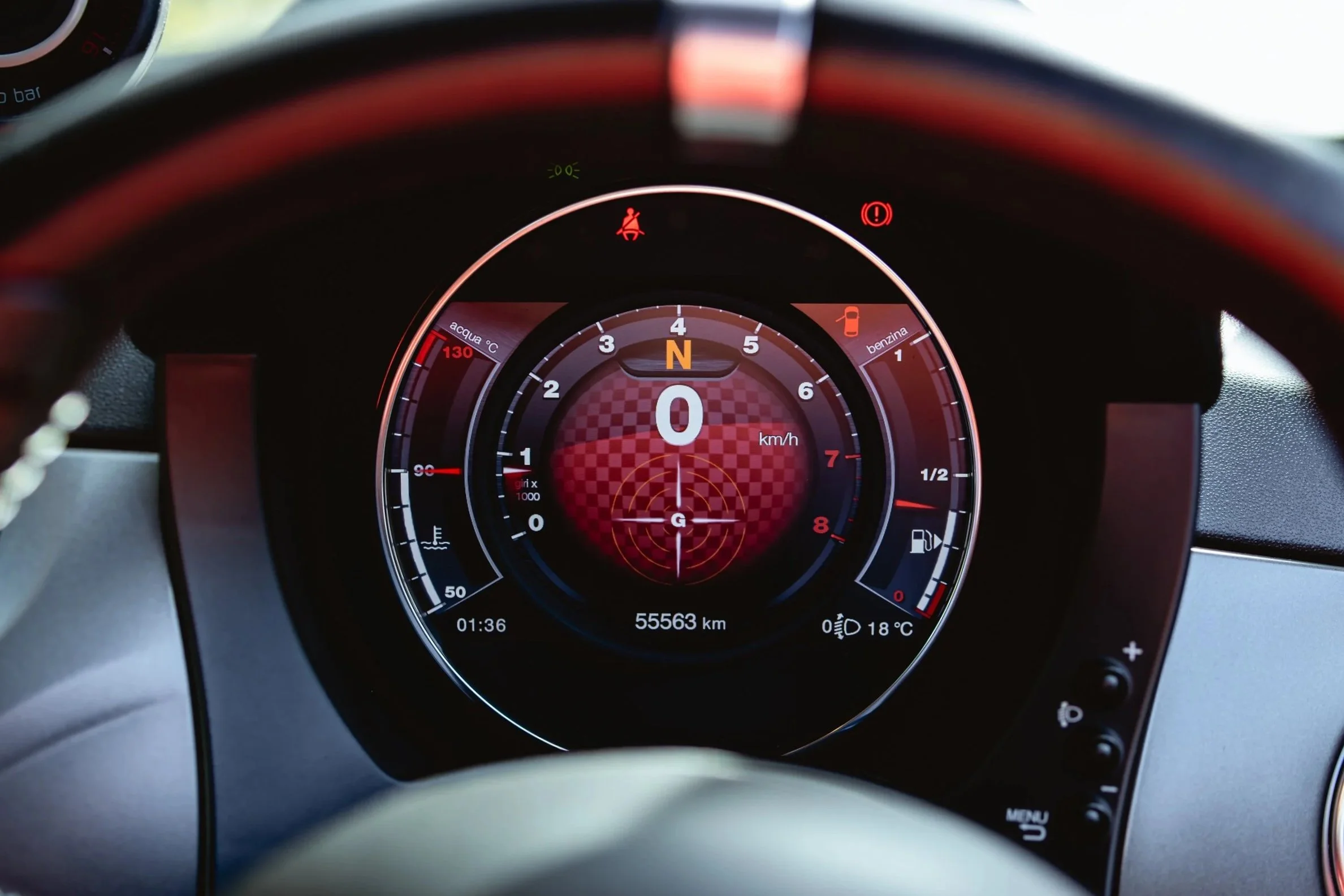 Car dashboard with digital speedometer at 0 km/h, odometer reading 55,563 km, and various warning indicators including seat belt, parking brake, fuel, and temperature gauges.