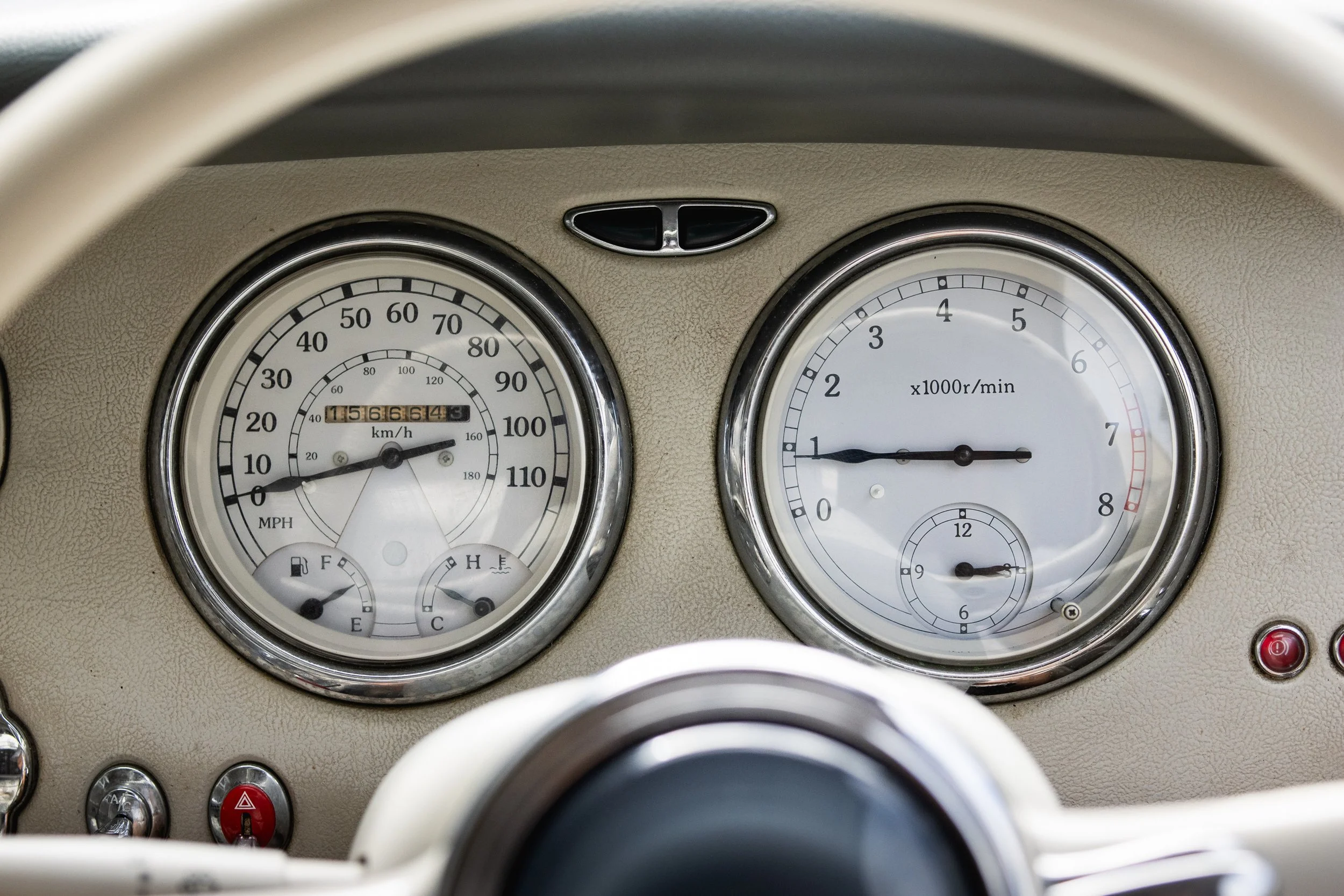 Close-up view of a vintage car dashboard with round speedometer on the left, tachometer on the right, and small gauges for fuel, temperature, and other indicators.
