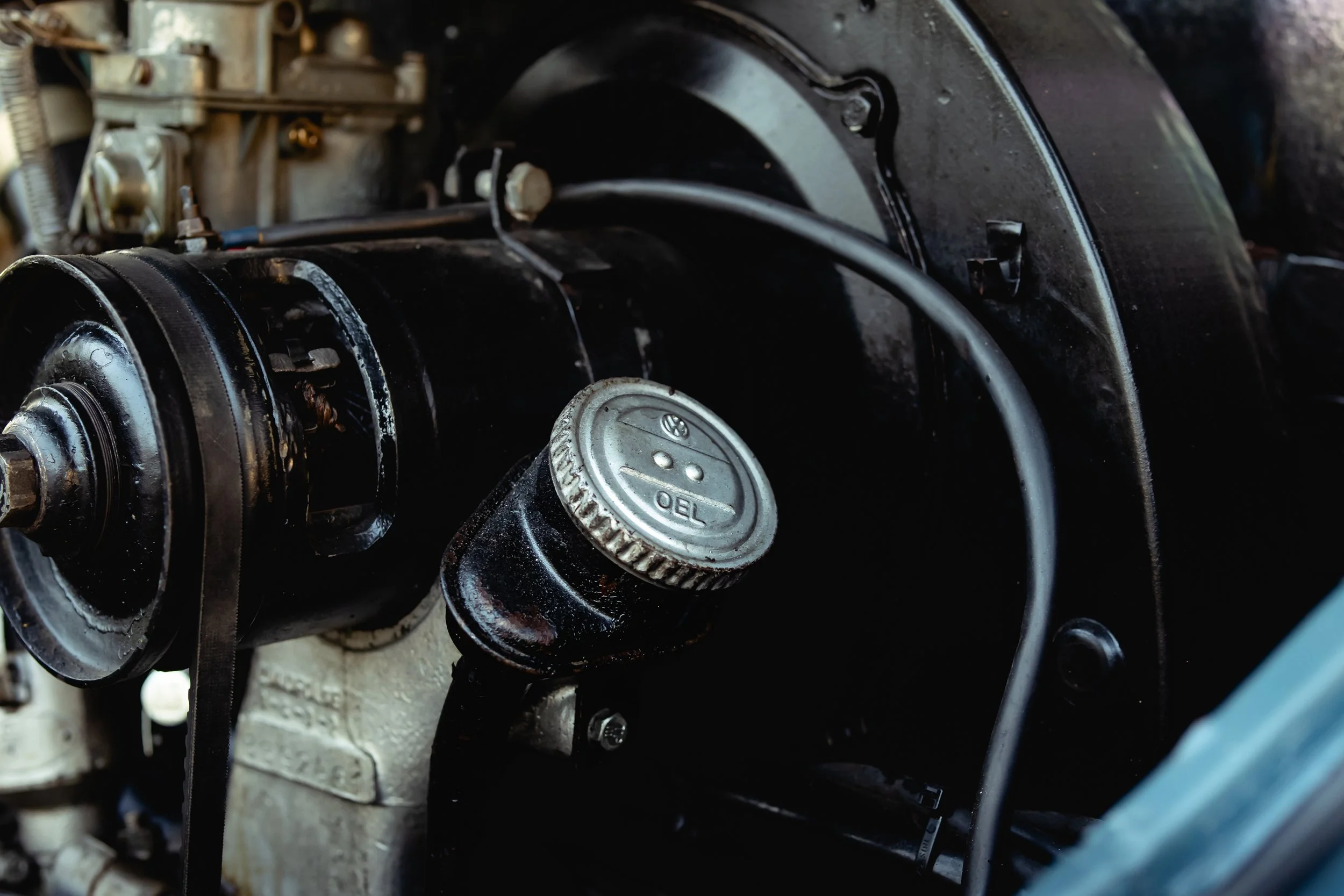 Close-up view of a vintage car engine with a focus on a silver oil cap and surrounding mechanical parts