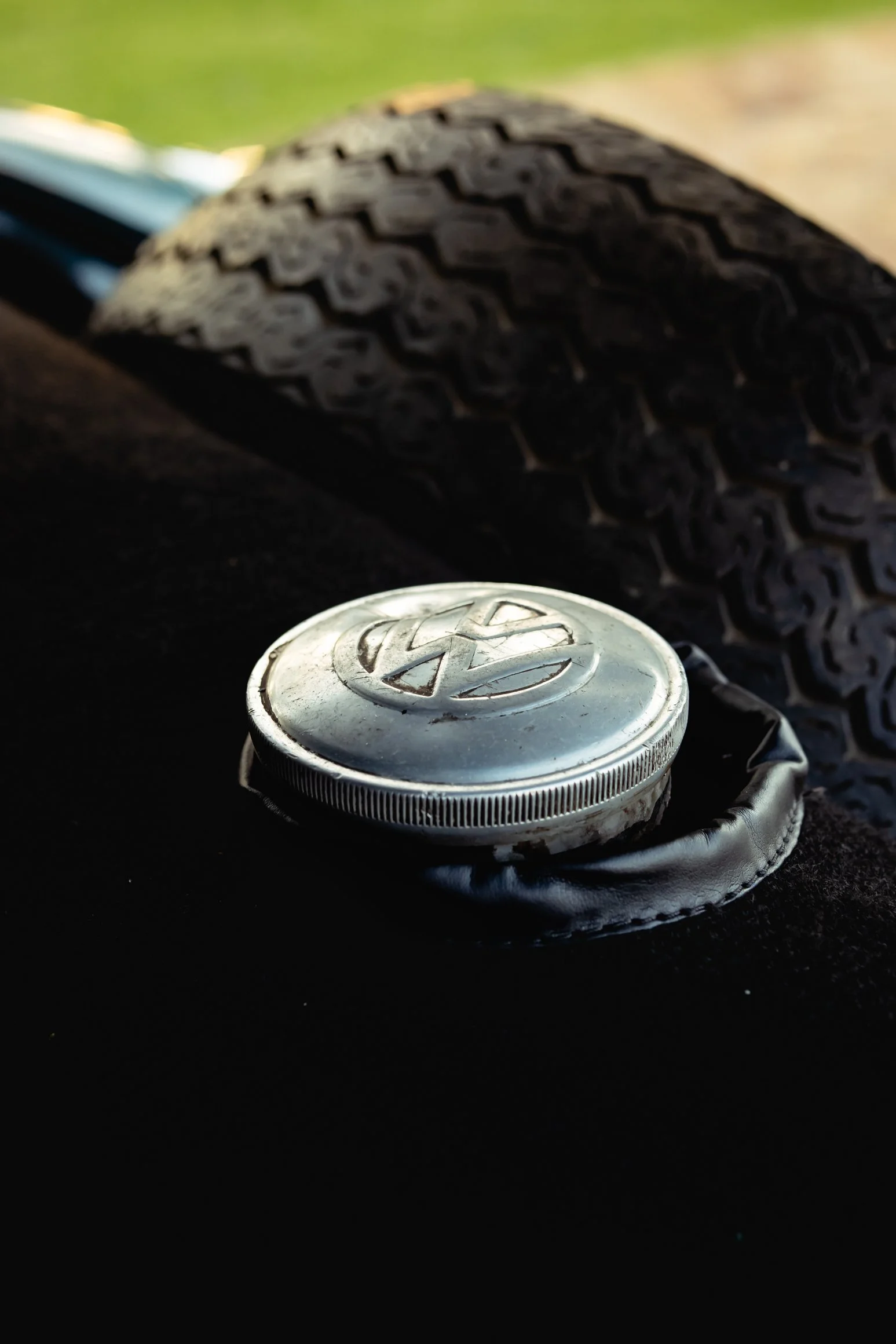 Close-up of a vintage Volkswagen hubcap with a tire in the background, resting on a black surface.