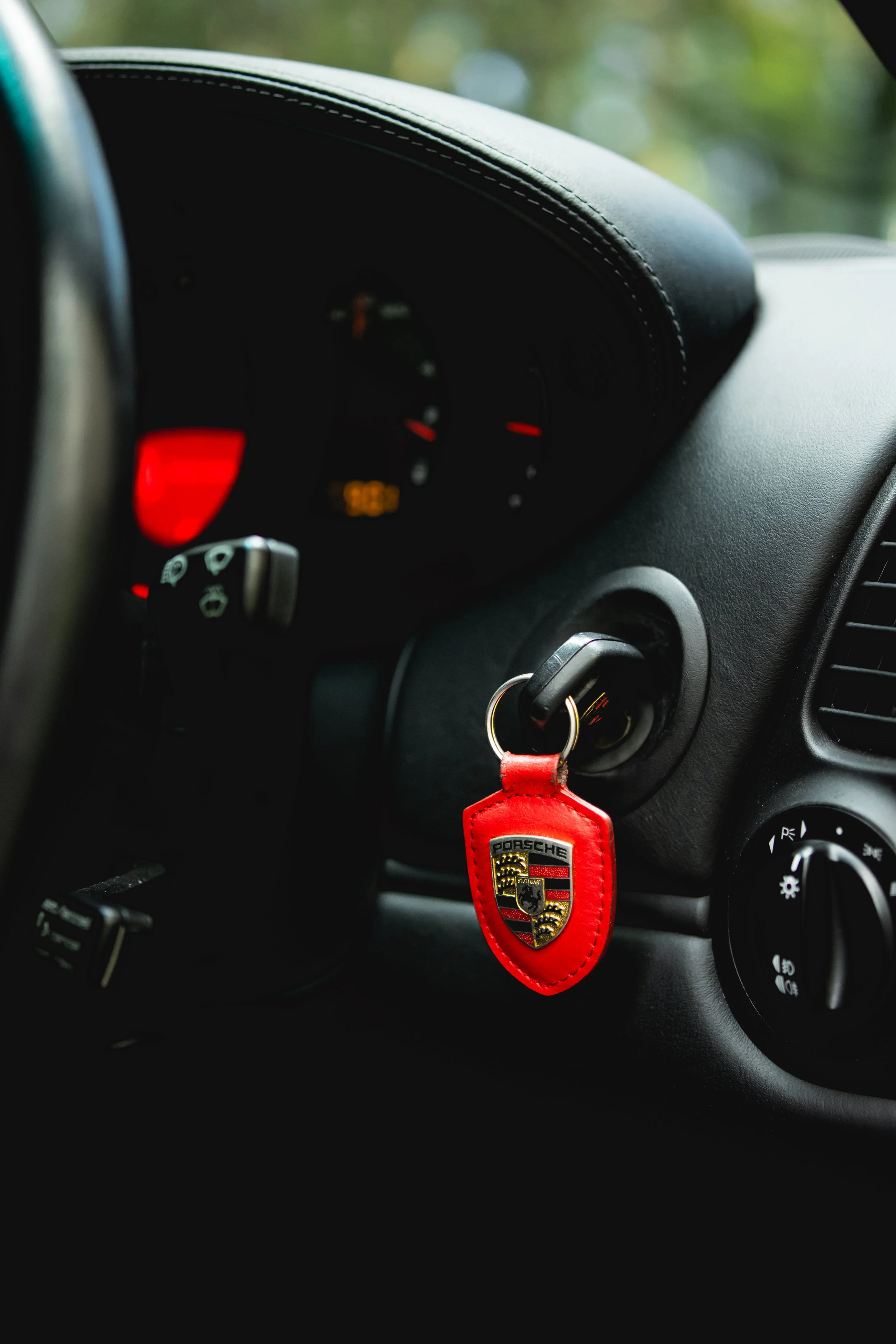 A close-up of a car's dashboard showing a Porsche keychain hanging from the ignition switch.
