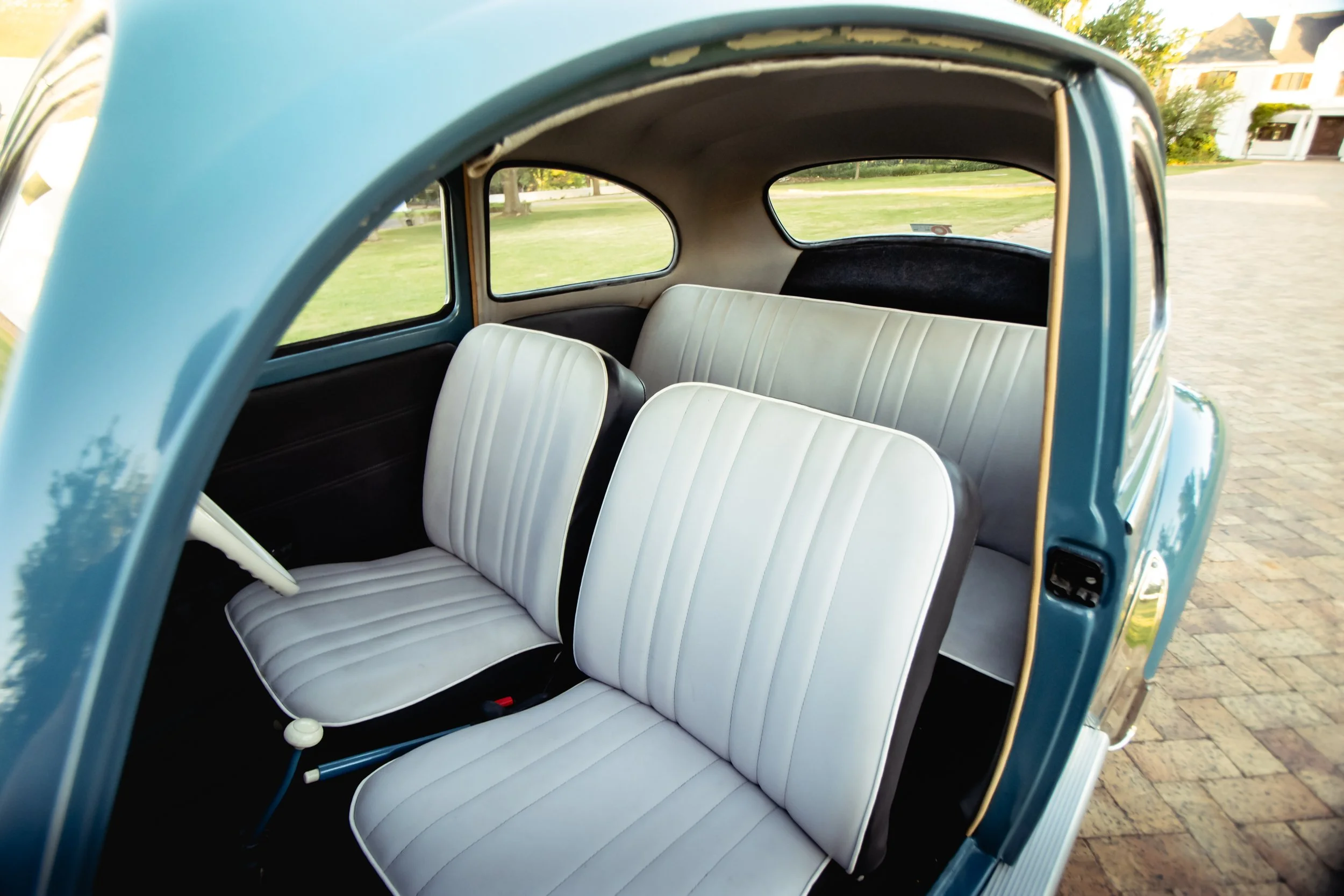 Interior view of a vintage blue car showing front and rear white padded seats.