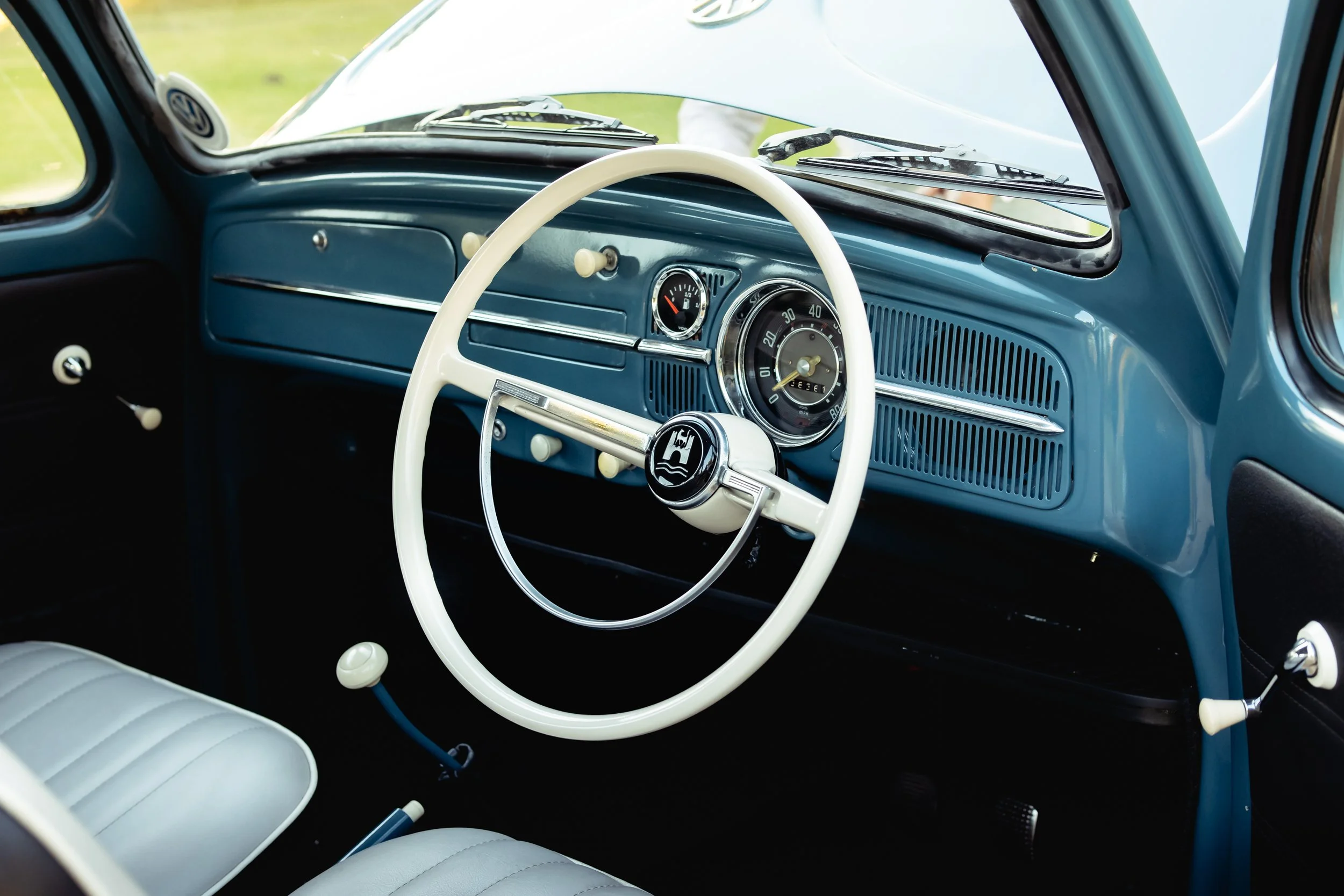 Interior of a vintage car showing a blue dashboard, white steering wheel, and vintage gauges.