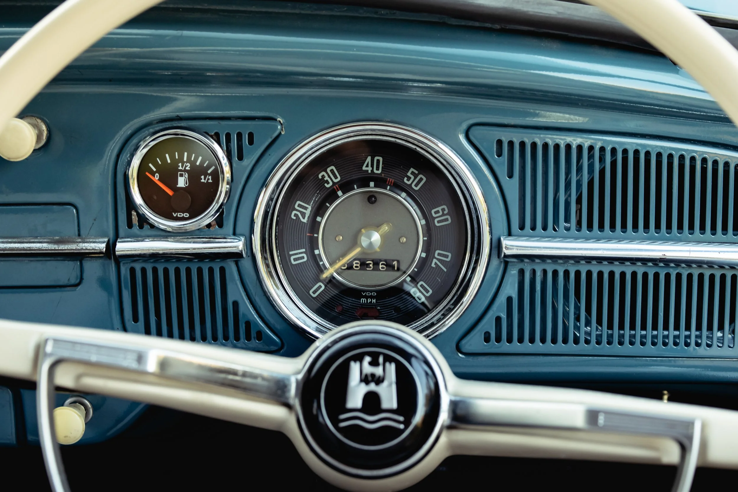 The dashboard of a vintage car featuring a speedometer, fuel gauge, and steering wheel with emblem.