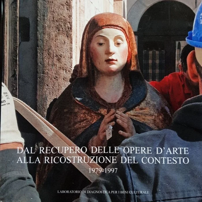 Statua di una donna con abito storico, con le mani in una posizione di preghiera, circondata da persone. Scritto in italiano: 'Dal recupero delle opere d'arte alla ricostruzione del contesto 1979-1997. Laboratorio di diagnostica per i beni culturali'.