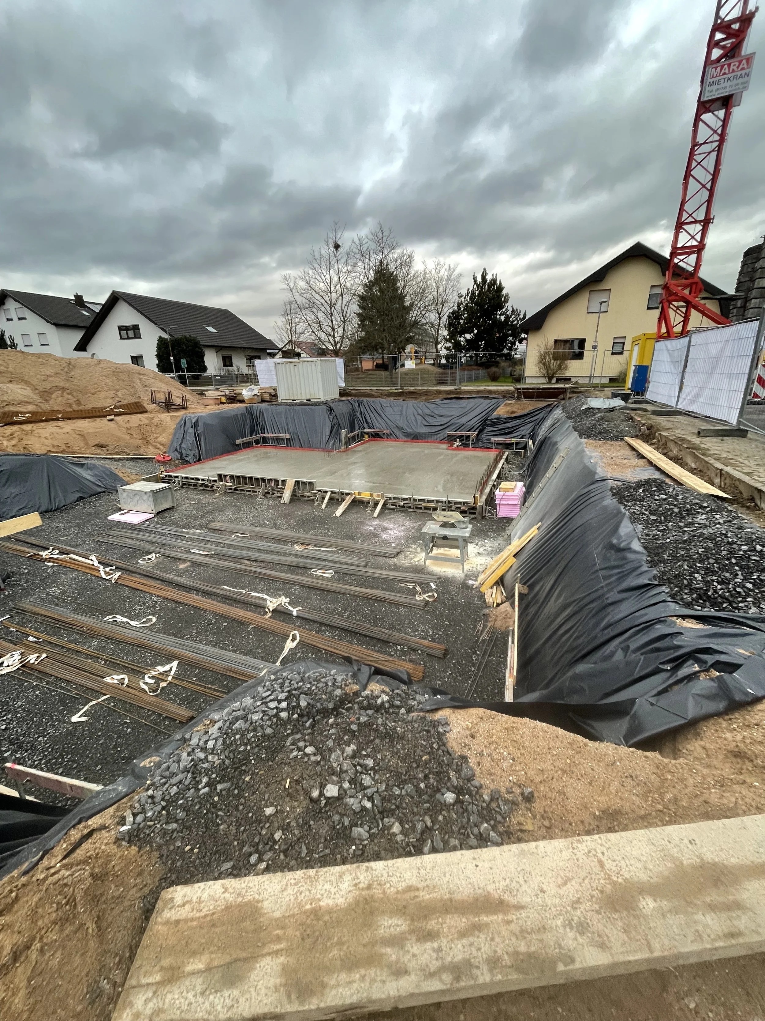 Baustelle mit Fundament und Baugerüst, Wolkenhimmel, umliegende Häuser, Baugerät