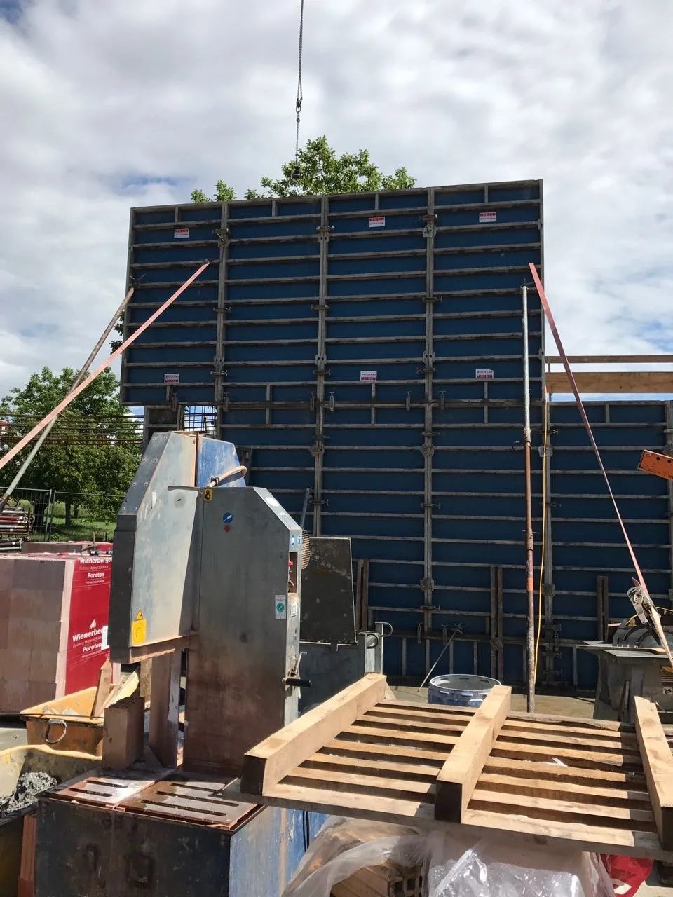Baustelle mit Baugerüst und Holzplatten, Baugeräte und Materialien, im Hintergrund Bäume und bewölkter Himmel