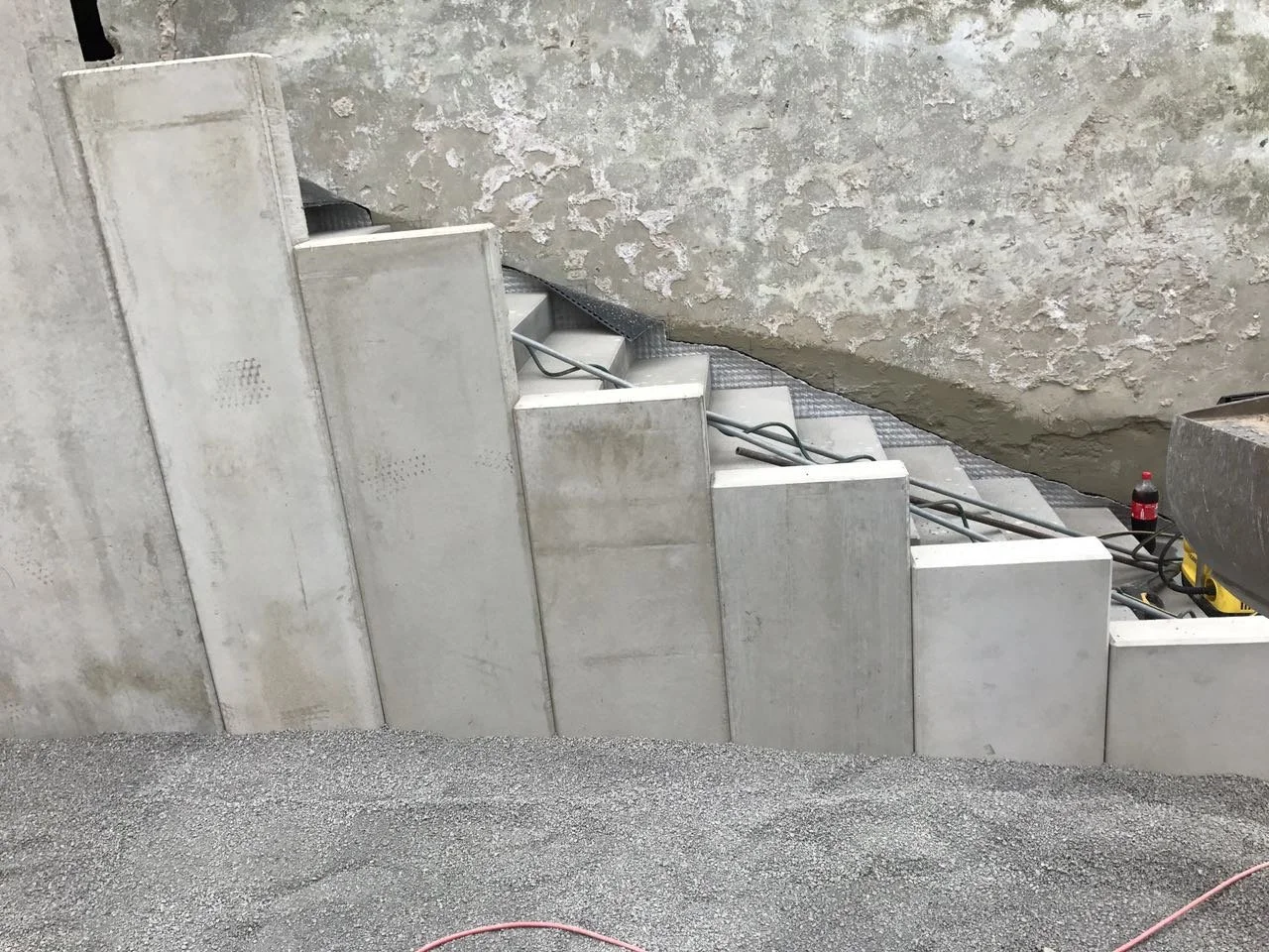 Betonstufen im Bau, mit sichtbaren Kabeln und Baustellenmaterial, vor einer betonierten Wand.