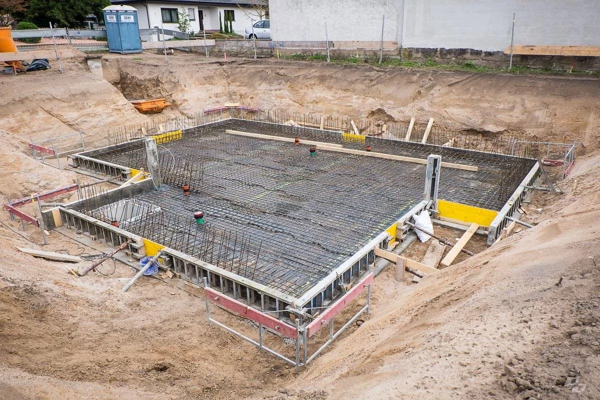 Fundament eines Gebäudes im Bau mit Stahlbewehrung und Schalung, umgeben von Erdreich.
