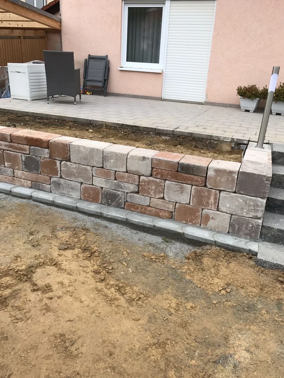 Bau einer terrassenförmigen Mauer aus Ziegelsteinen vor einem Haus mit Terrasse, die mit Pflastersteinen gepflastert ist.