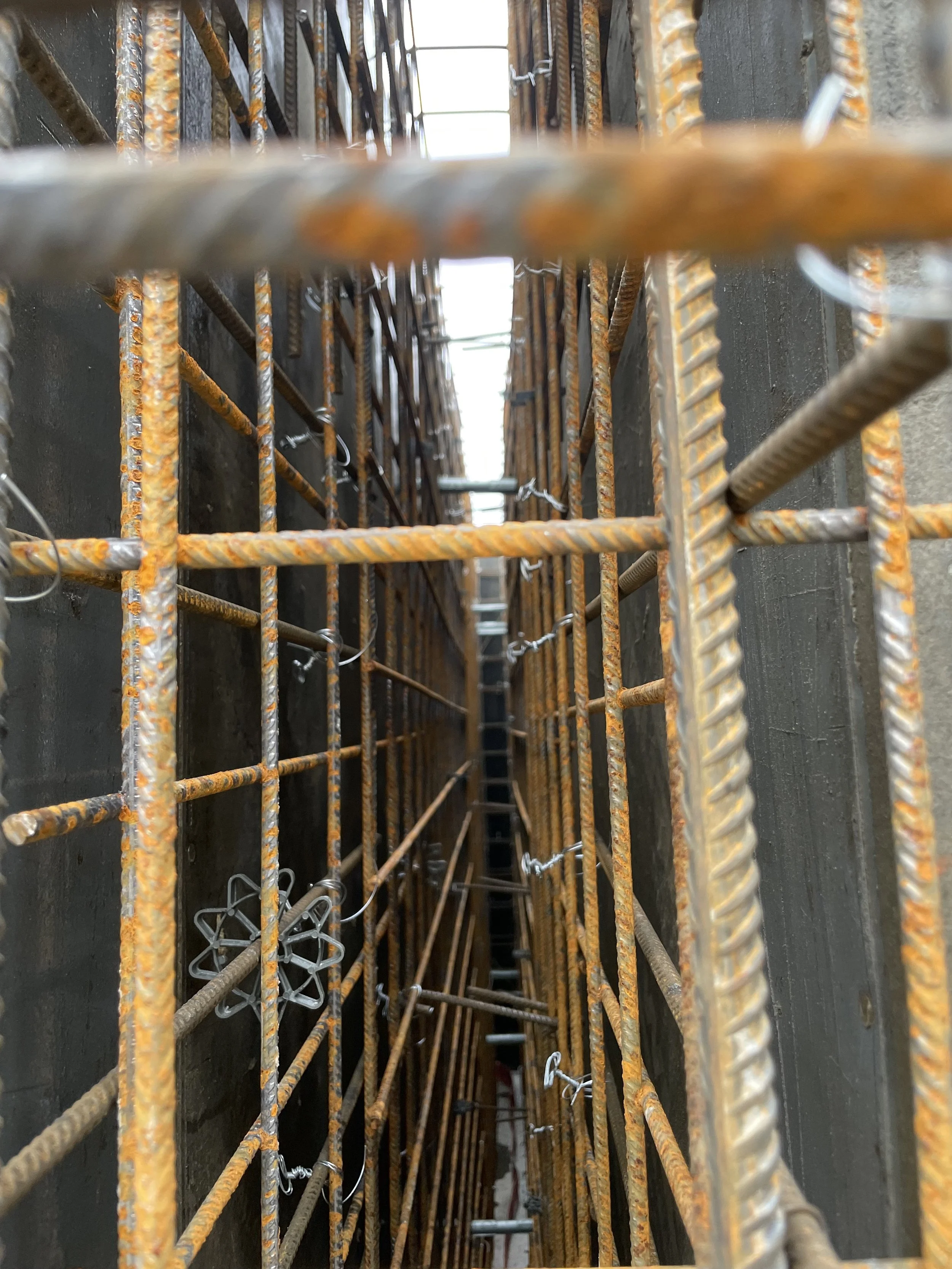 Blick durch ein Gitter aus rostigem Eisen, das auf einer Baustelle verwendet wird, mit einem vertikalen Tunnel zwischen den Gitterstäben.