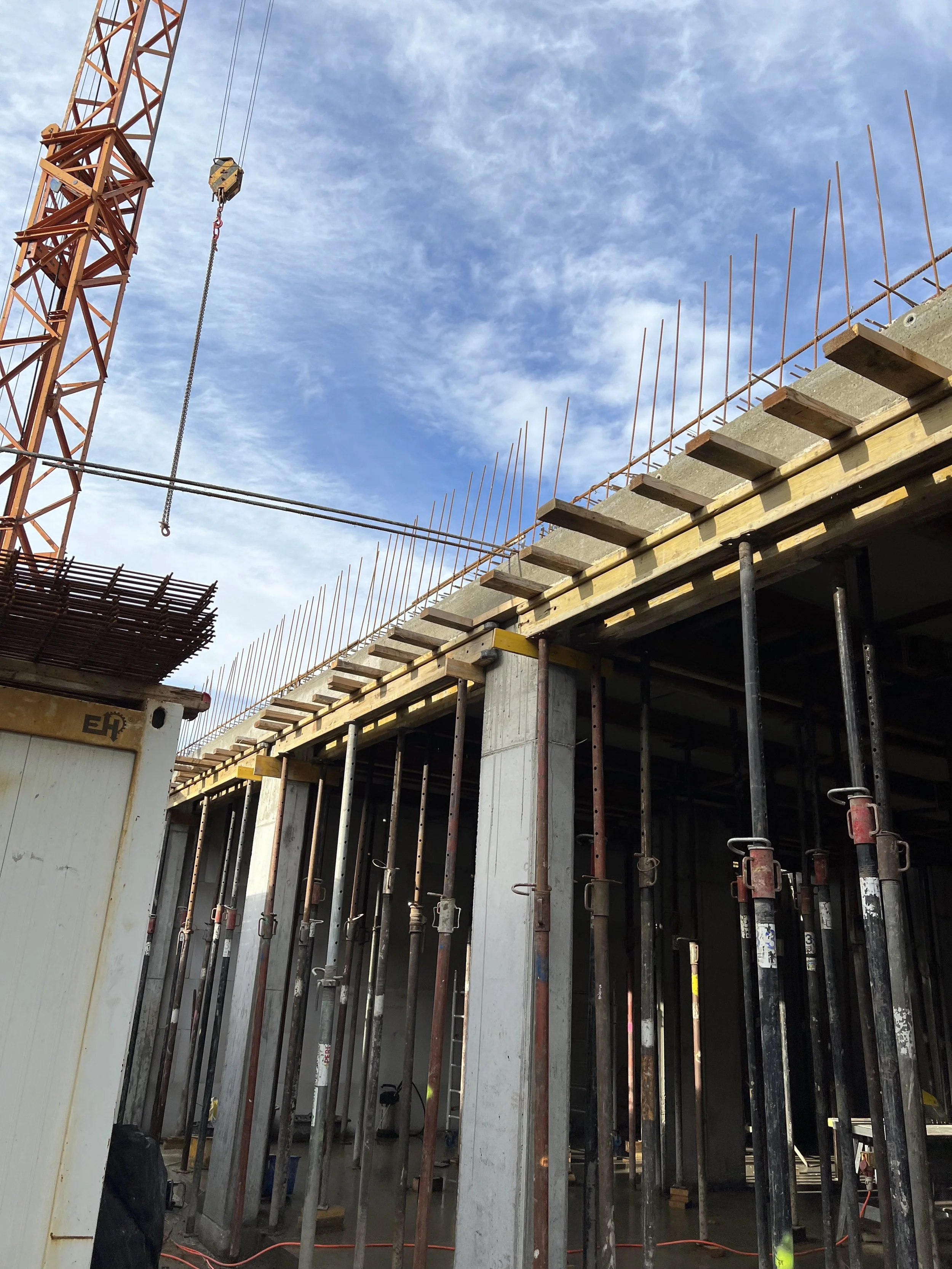 Baustelle mit Baugerüsten, Stahlstützen und einem Baukran im Himmel.