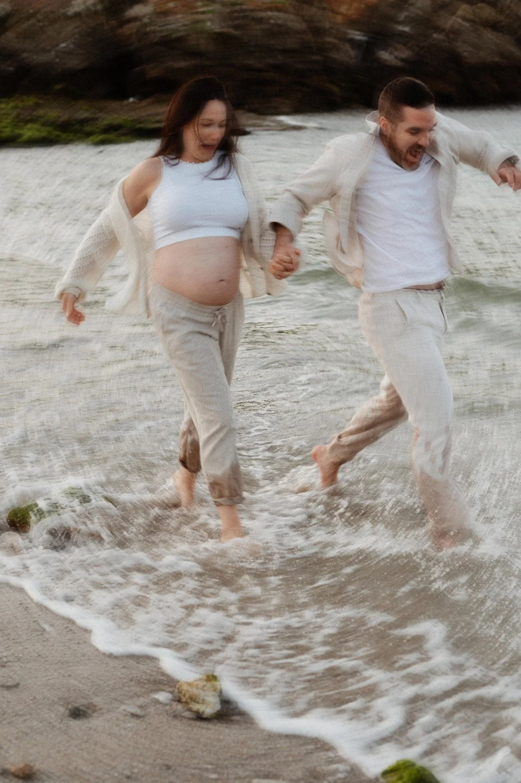 a soft-focus shot of a couple holding hands, running through the water along the beach, their trousers completely soaked