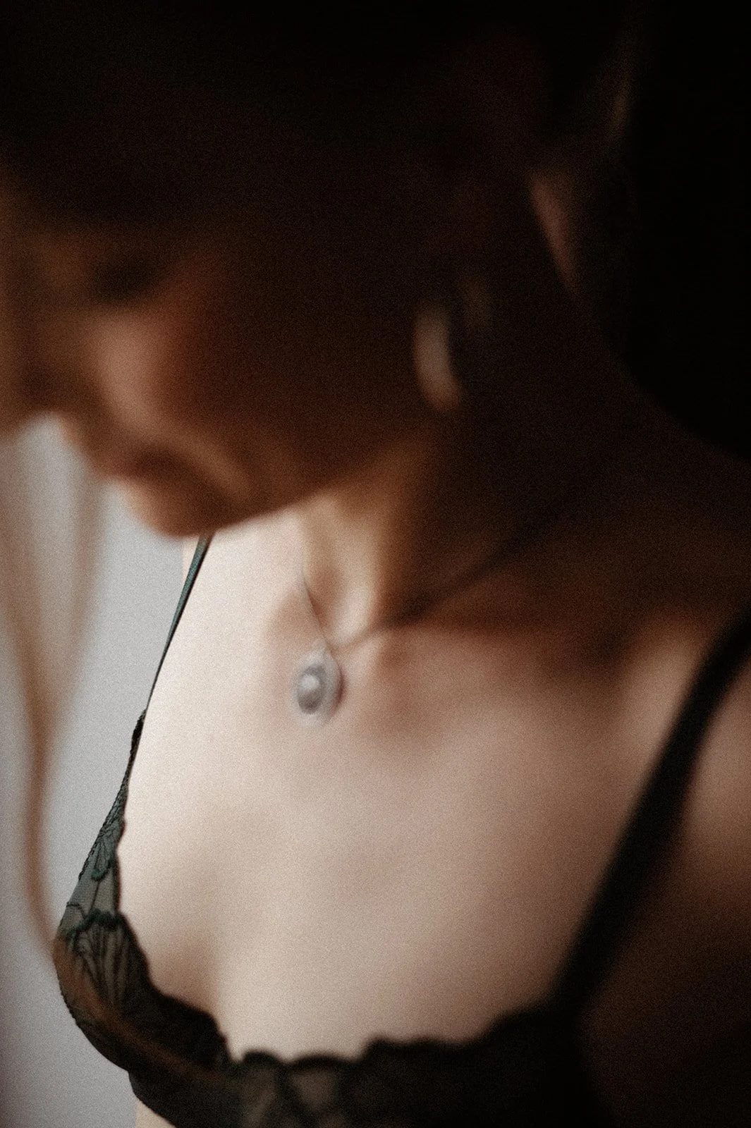 Close-up of a woman wearing black lingerie, with focus on her cleavage and a necklace with a round pendant.