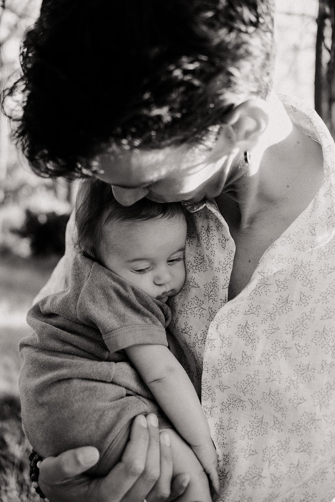 A black and white photograph of a father holding his newborn close to his chest, with the father gently kissing the child's head.