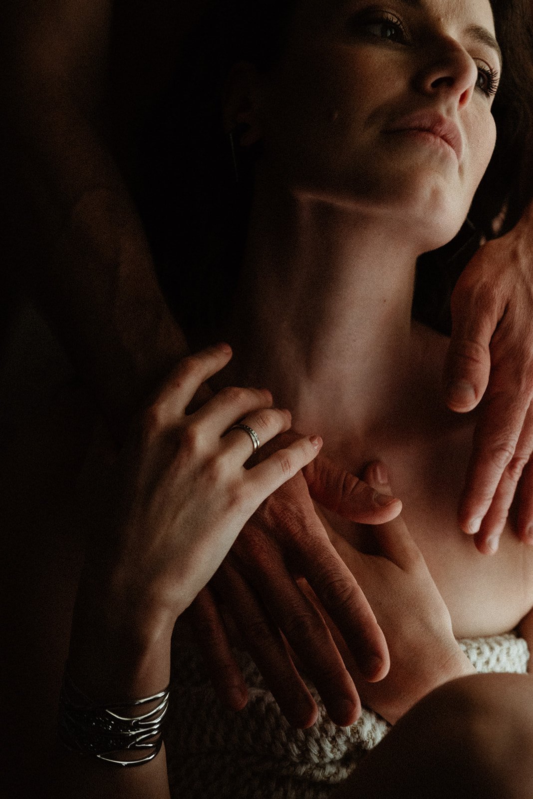 Close-up of multiple hands touching a woman's bare chest in an intimate setting, with the woman's face partially visible and serene.