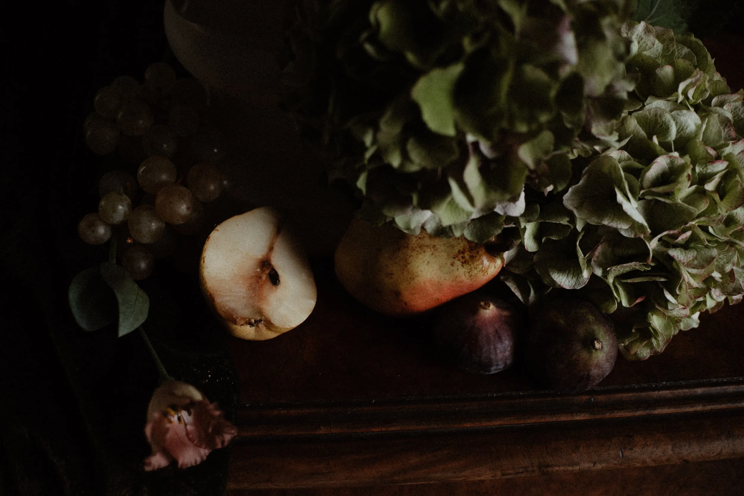 Dark image of assorted fruits and vegetables including grapes, apples, figs, and leafy greens.