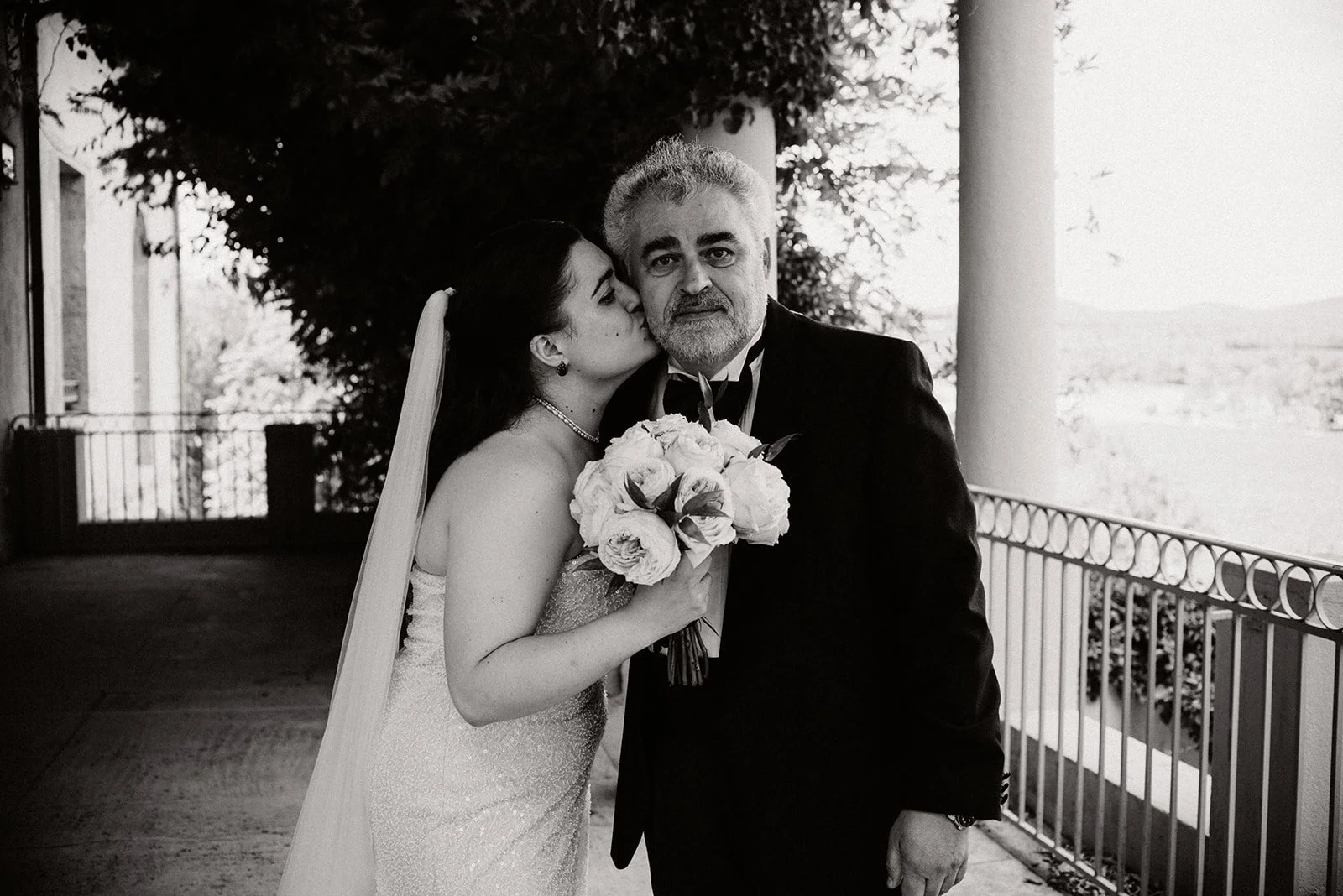 Black and white photo of a bride kissing her deeply moved father on the cheek during a first look