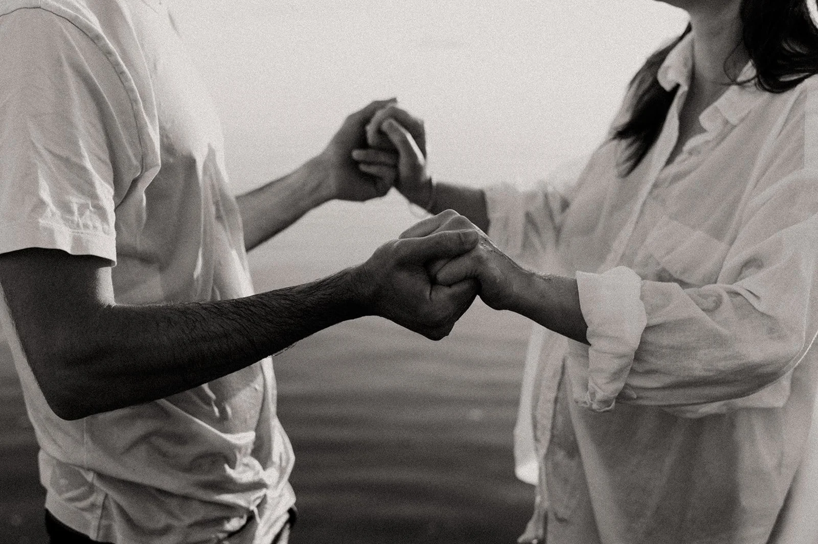 Close-up of a couple facing each other, holding hands, at sunset on the beach, black-and-white photo