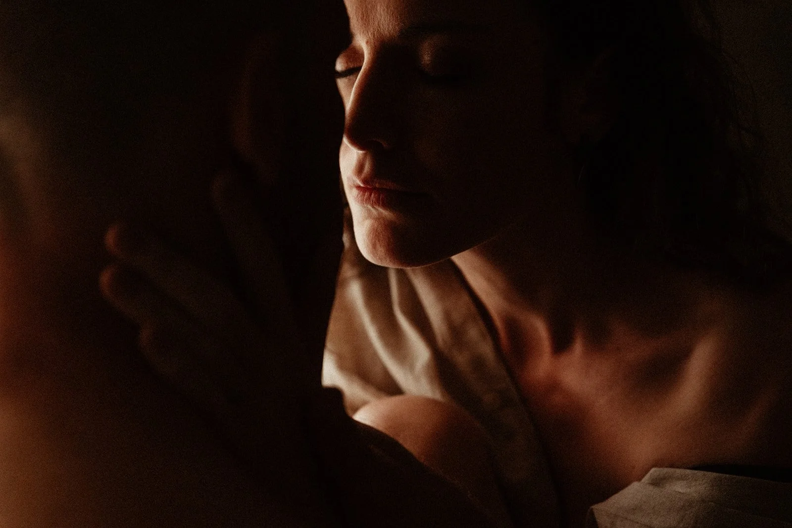 A woman with closed eyes gently touching the forehead of her partner in a dimly lit, intimate setting.