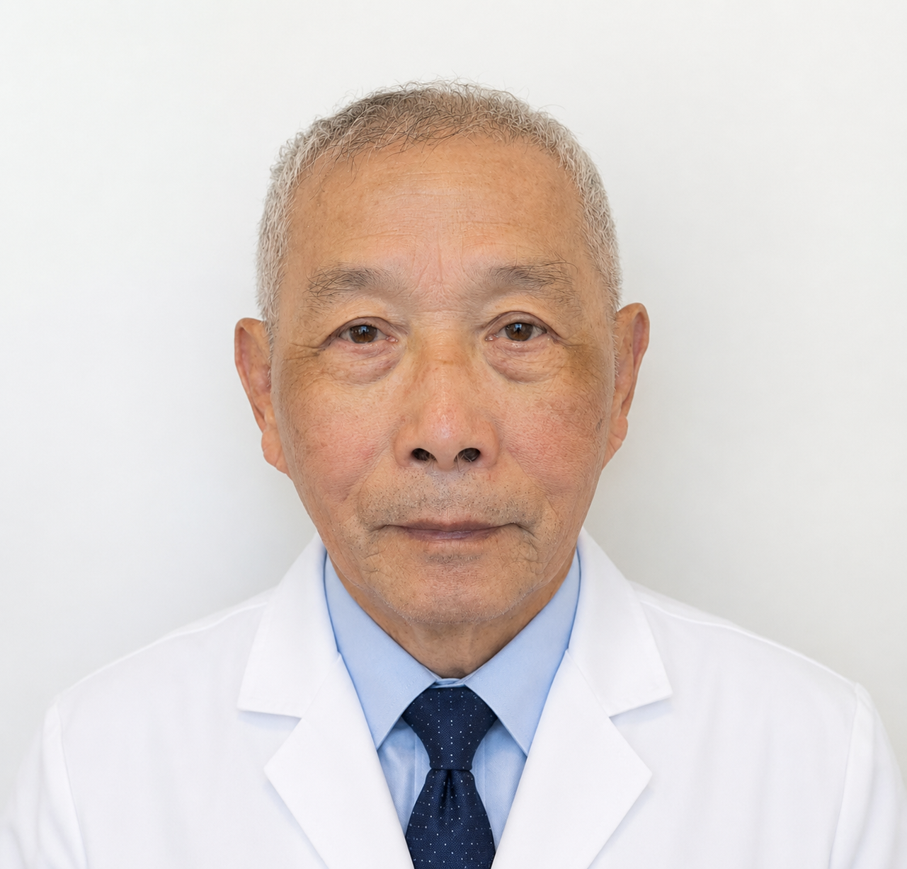 An elderly Asian man with short gray hair, wearing a white lab coat, light blue dress shirt, and dark blue tie, standing against a plain white background.