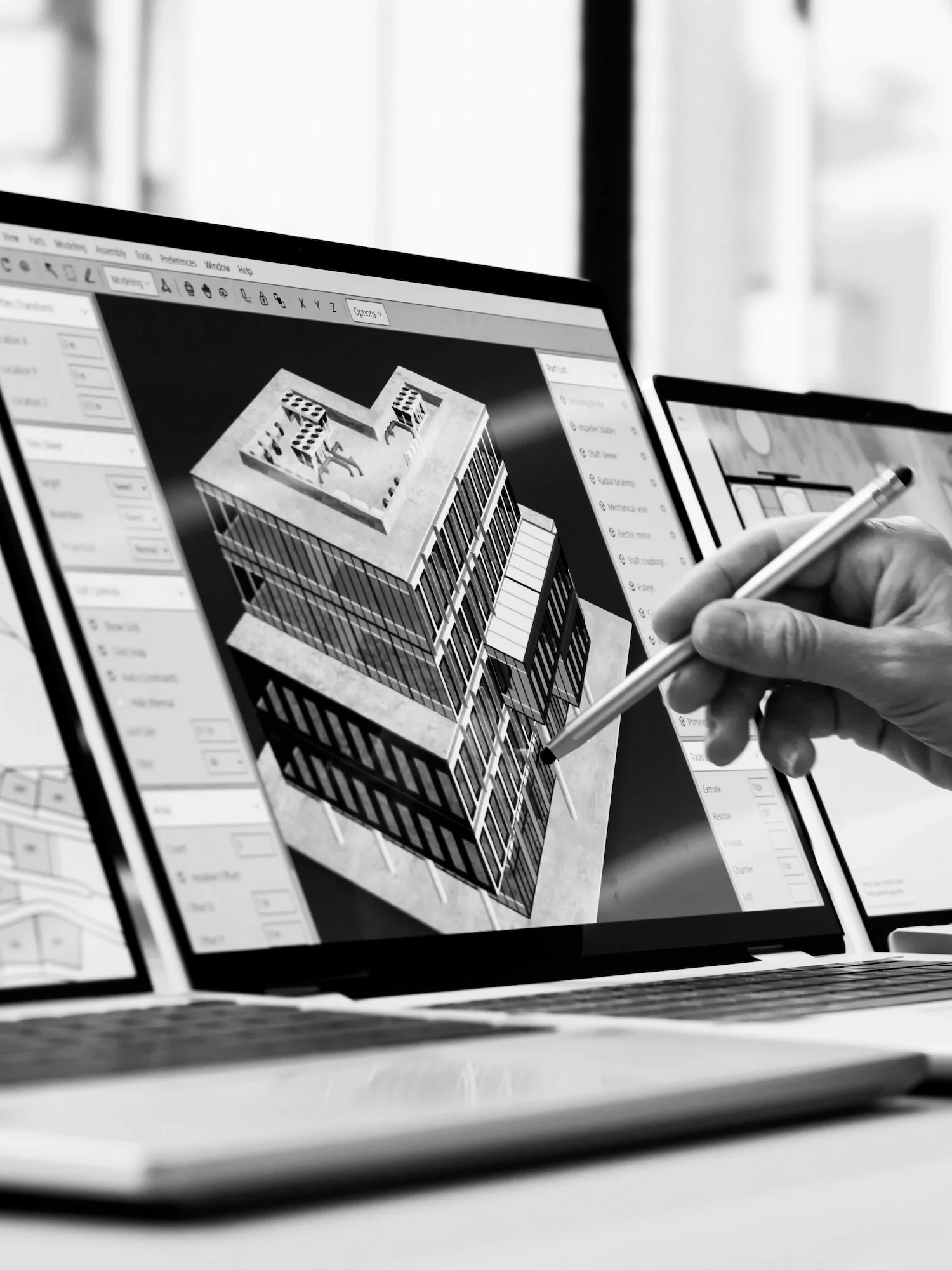 Black and white close-up of a hand using a stylus on a digital building model for construction
